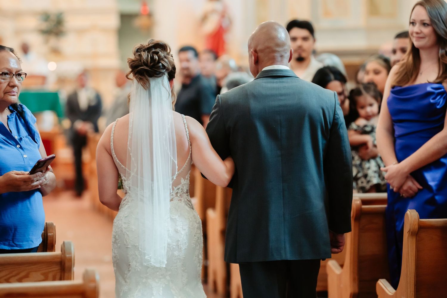 Wedding guests sitting in church pews during ceremony with soft lighting and interior decor visible.