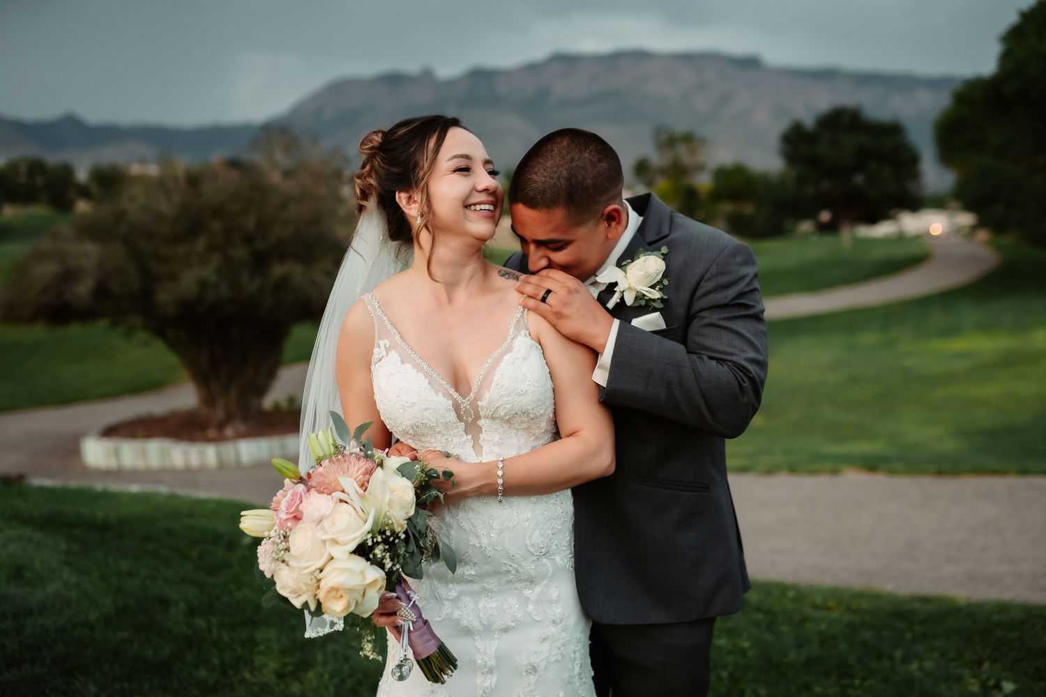 Wedding photograph captured on green hillside with scenic mountain backdrop and moody skies.