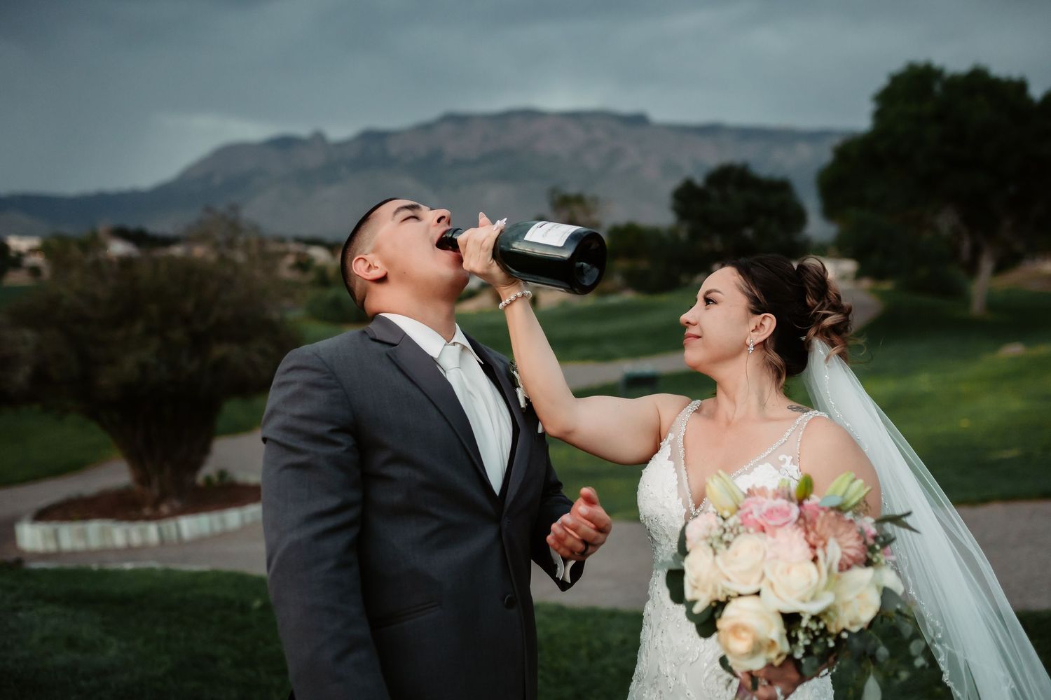 Wedding couple toasts with champagne against mountainous backdrop at sunset.