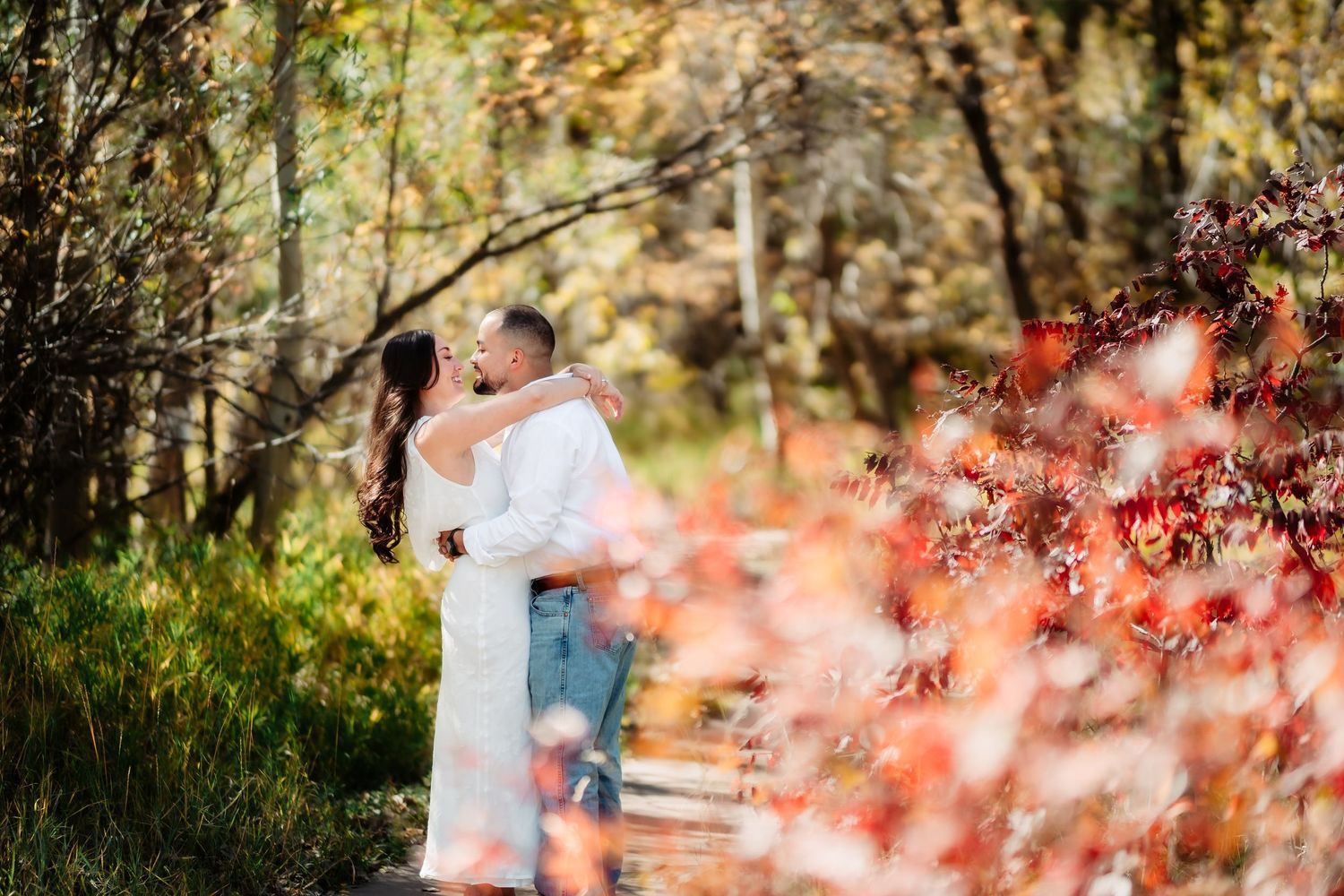 Couple sharing a romantic moment among autumn trees and pink blossoms in a park setting.