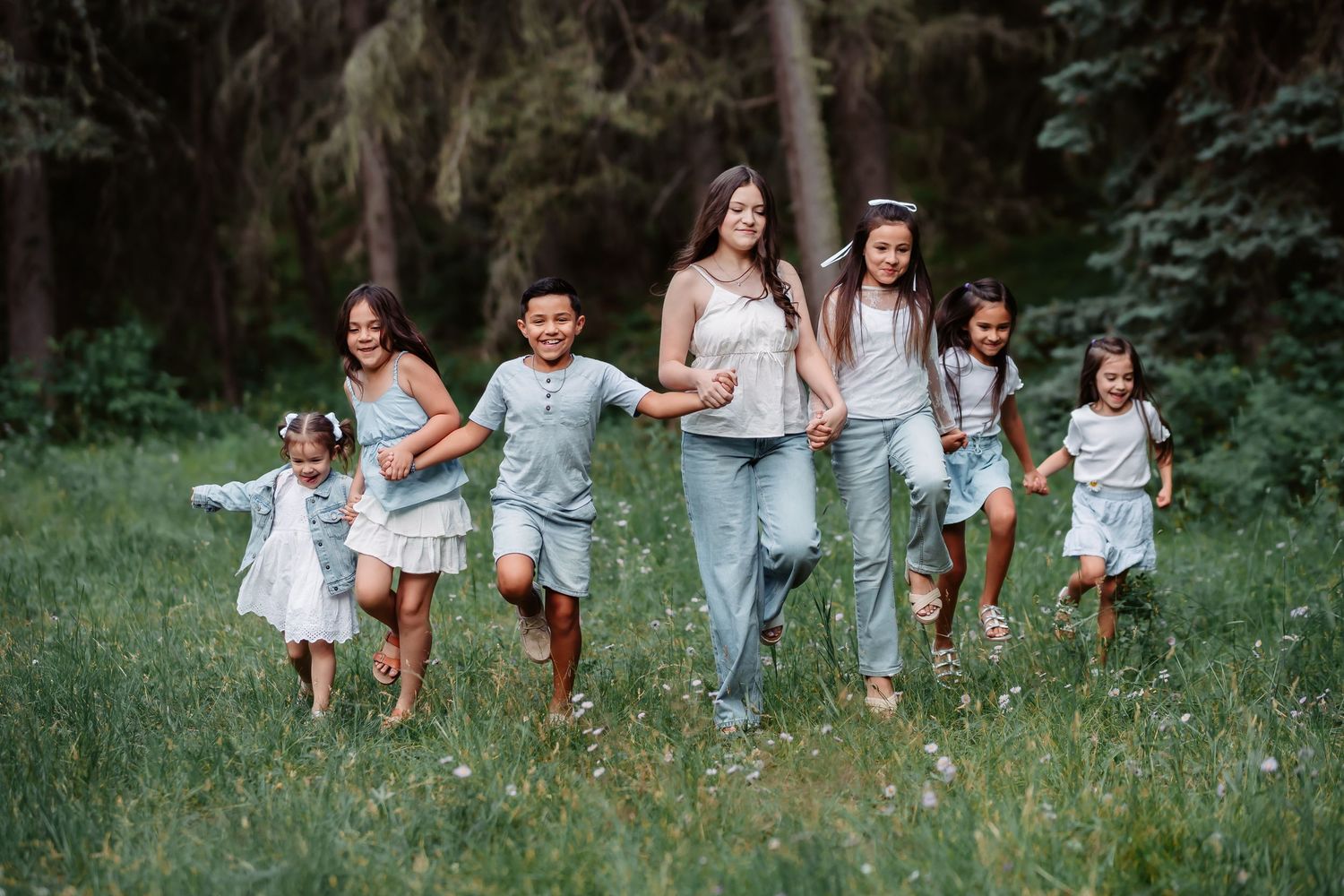 A group of people run joyfully through a lush green field surrounded by trees on a summer day.