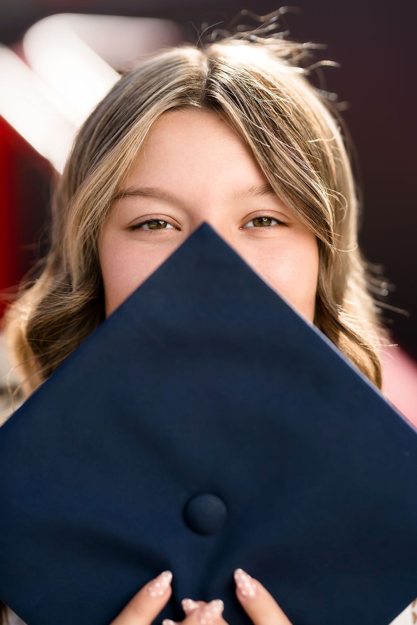 Smiling graduate peeks over navy blue graduation cap in close-up portrait photo.