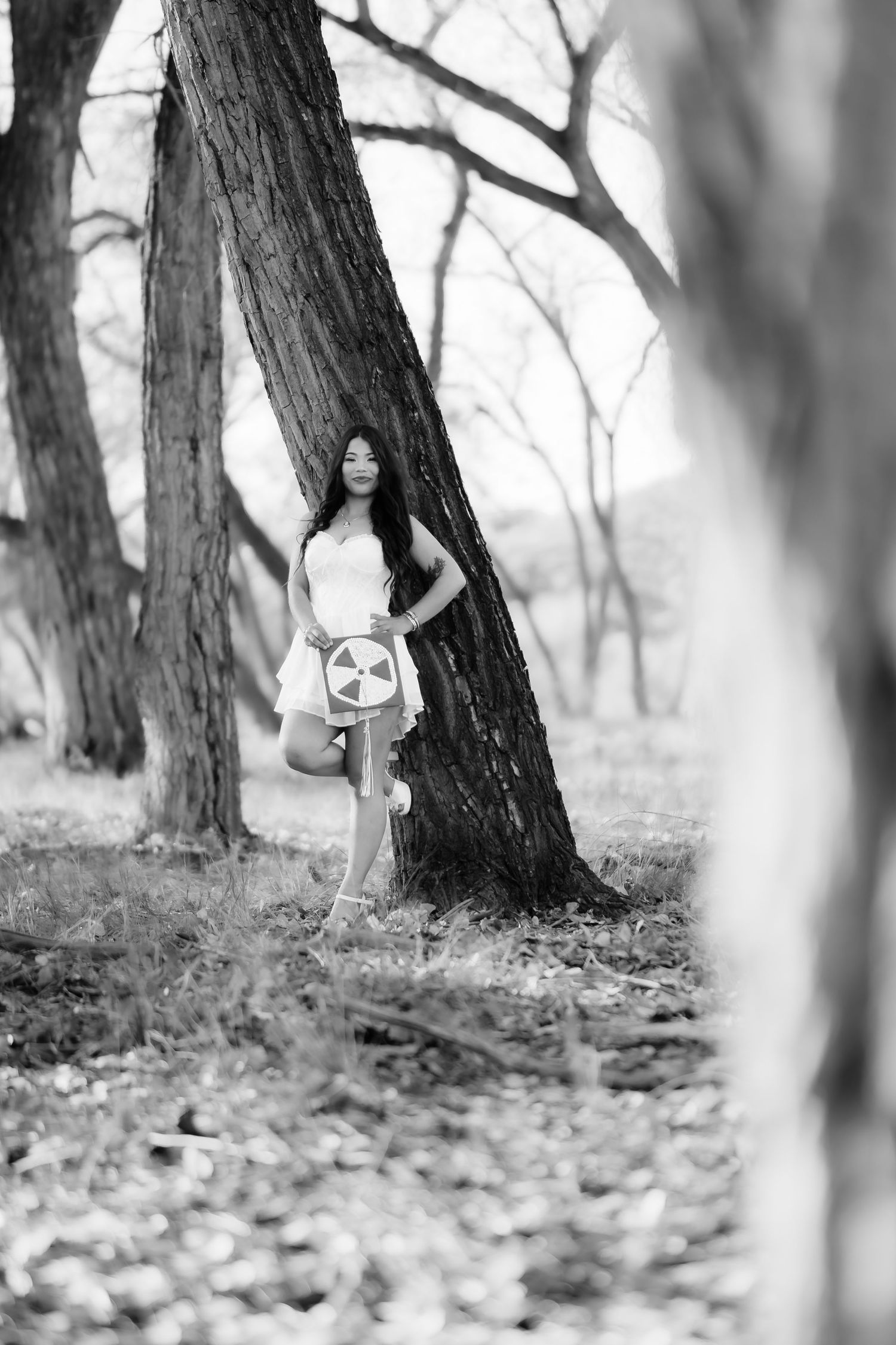 Black and white portrait of graduate posing between trees in natural outdoor setting.