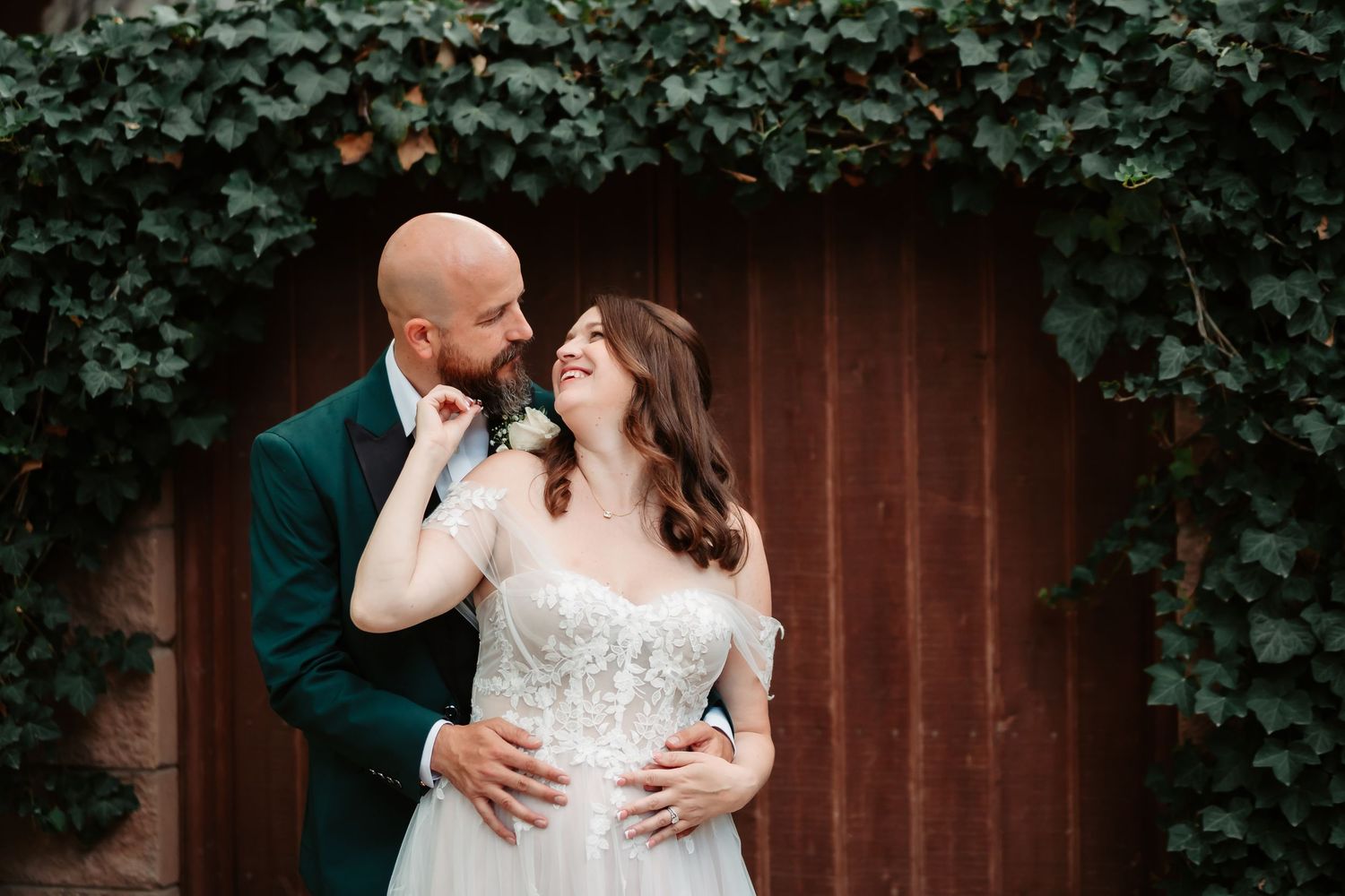 A couple shares an intimate moment in front of a wooden fence surrounded by lush green ivy.
