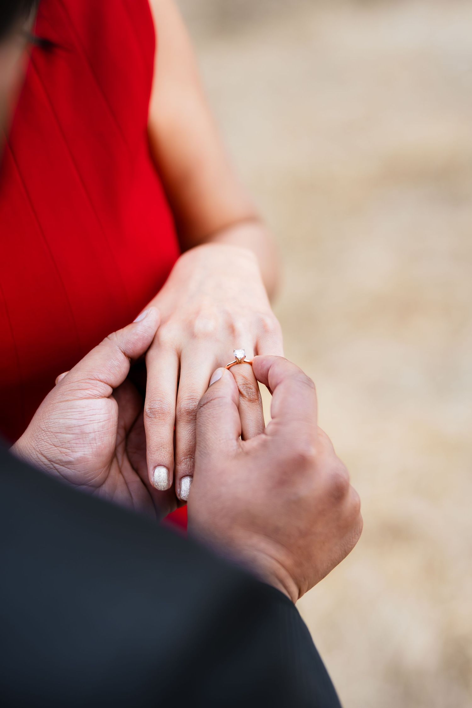 Close-up of hands during an engagement ring placement in an outdoor setting.
