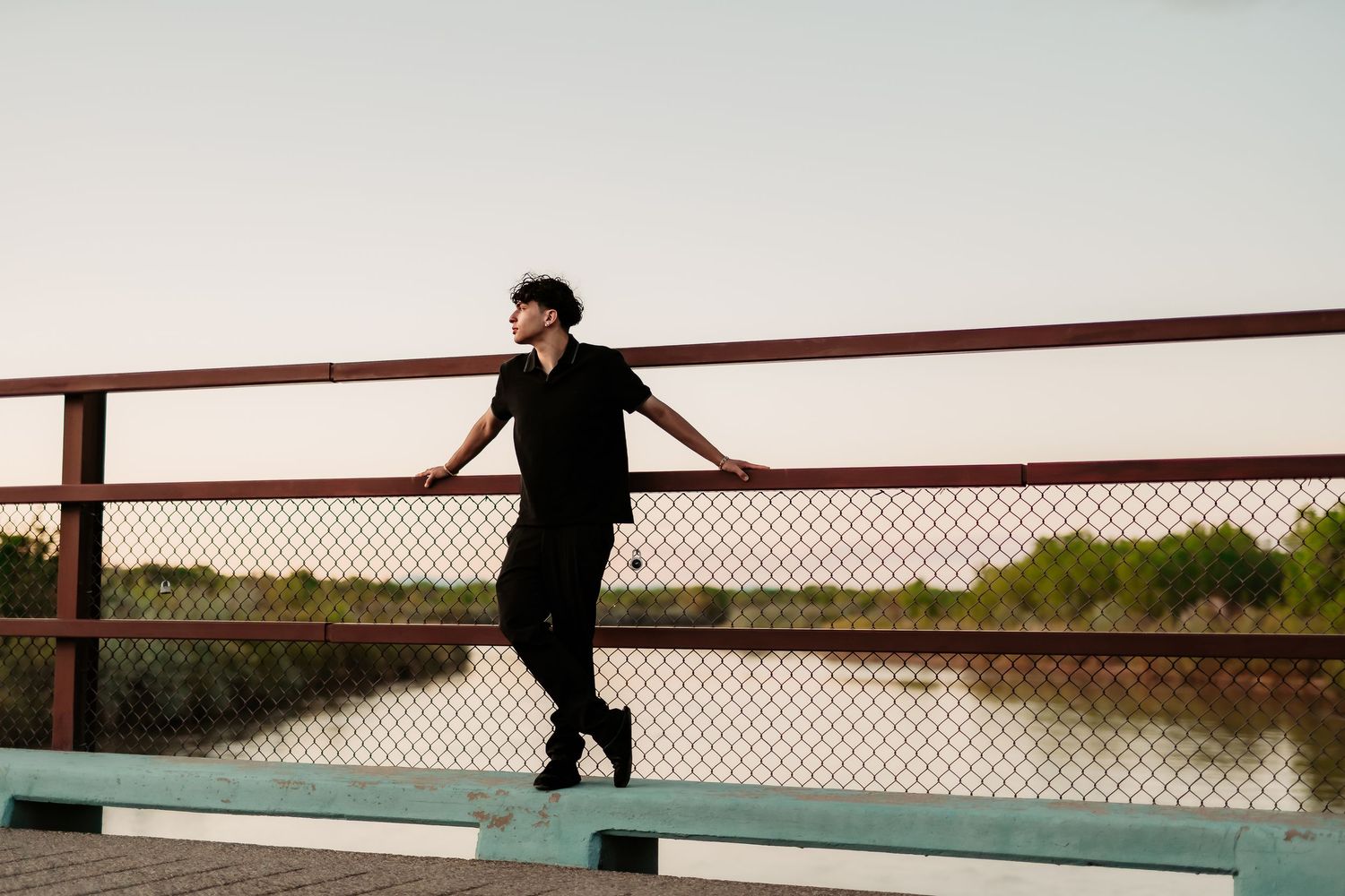 Artistic silhouette portrait on a railing with water and sunset in the background.