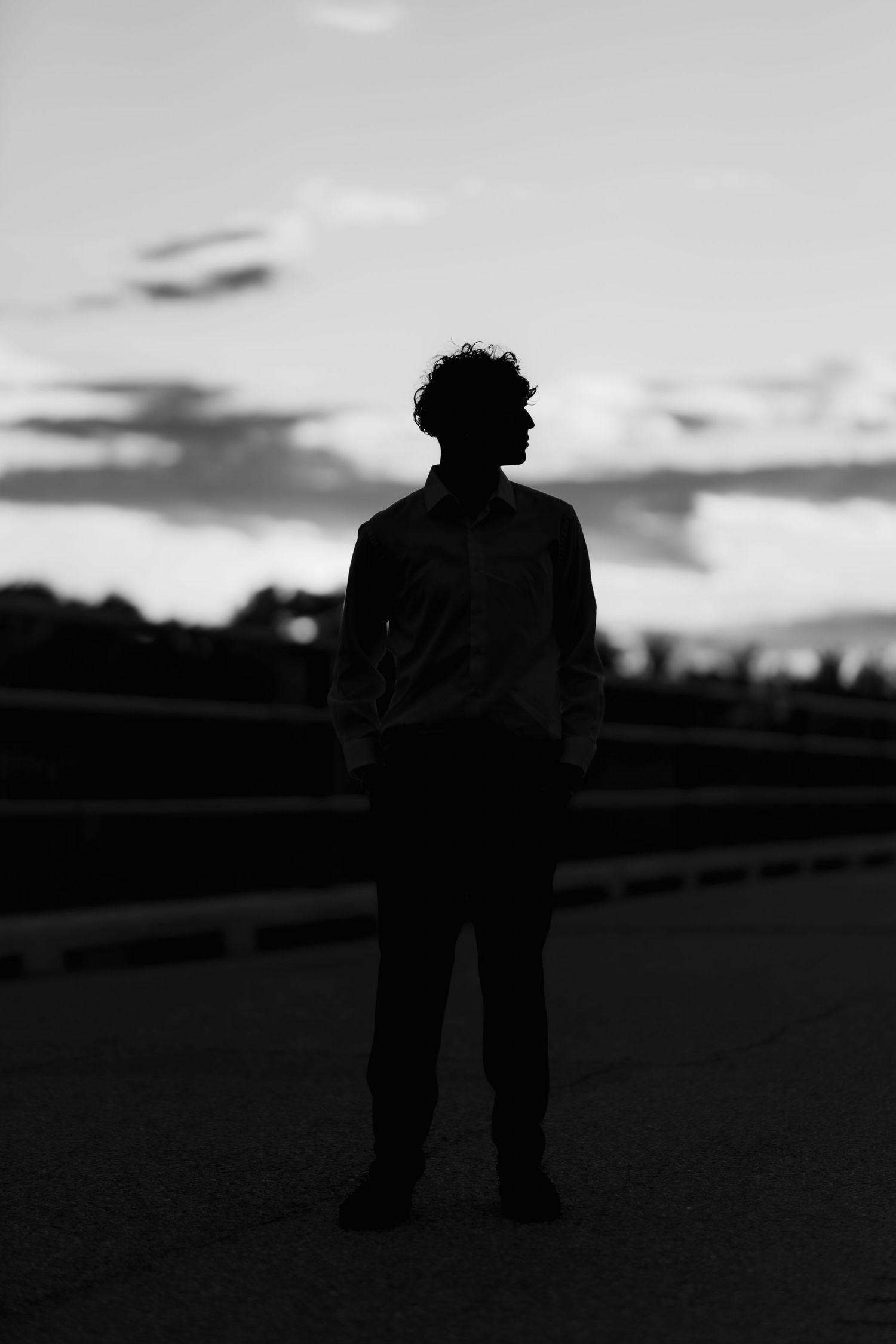 Black and white silhouette of a figure standing alone at dusk with clouds in the background.