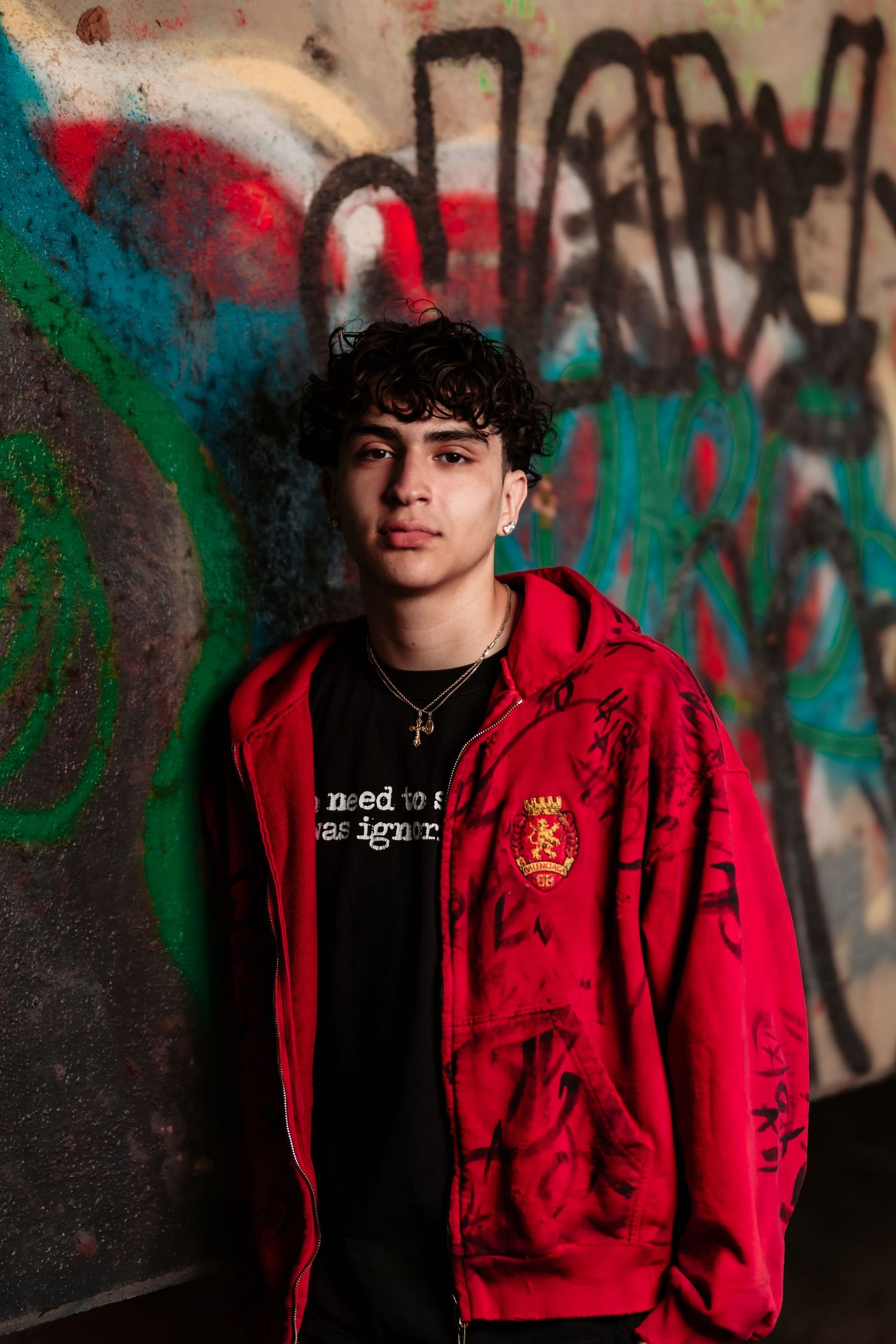 Fashion portrait against colorful graffiti wall featuring red hoodie and black t-shirt in urban setting.