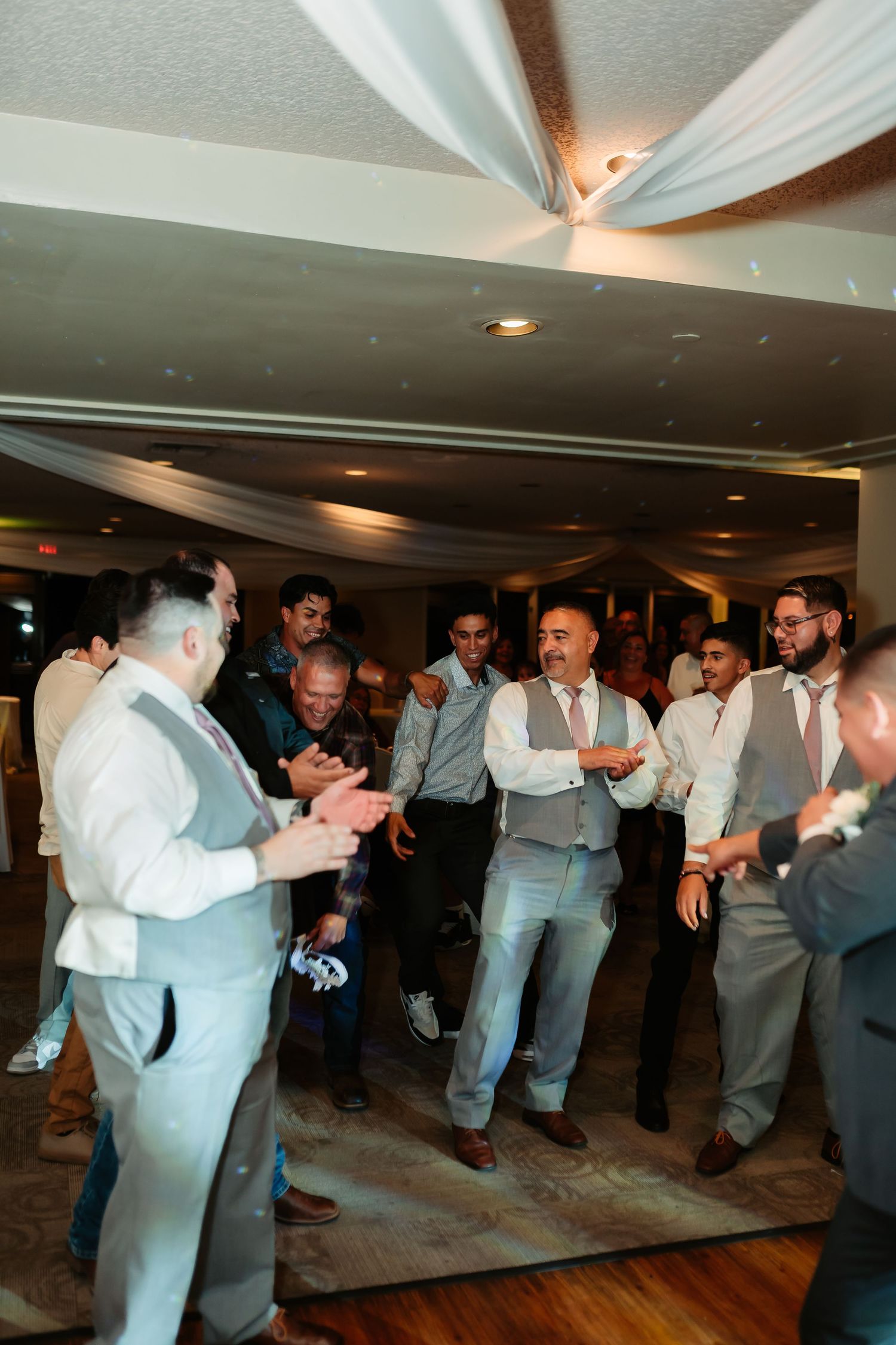 Large group of wedding guests performing synchronized dance moves at reception.