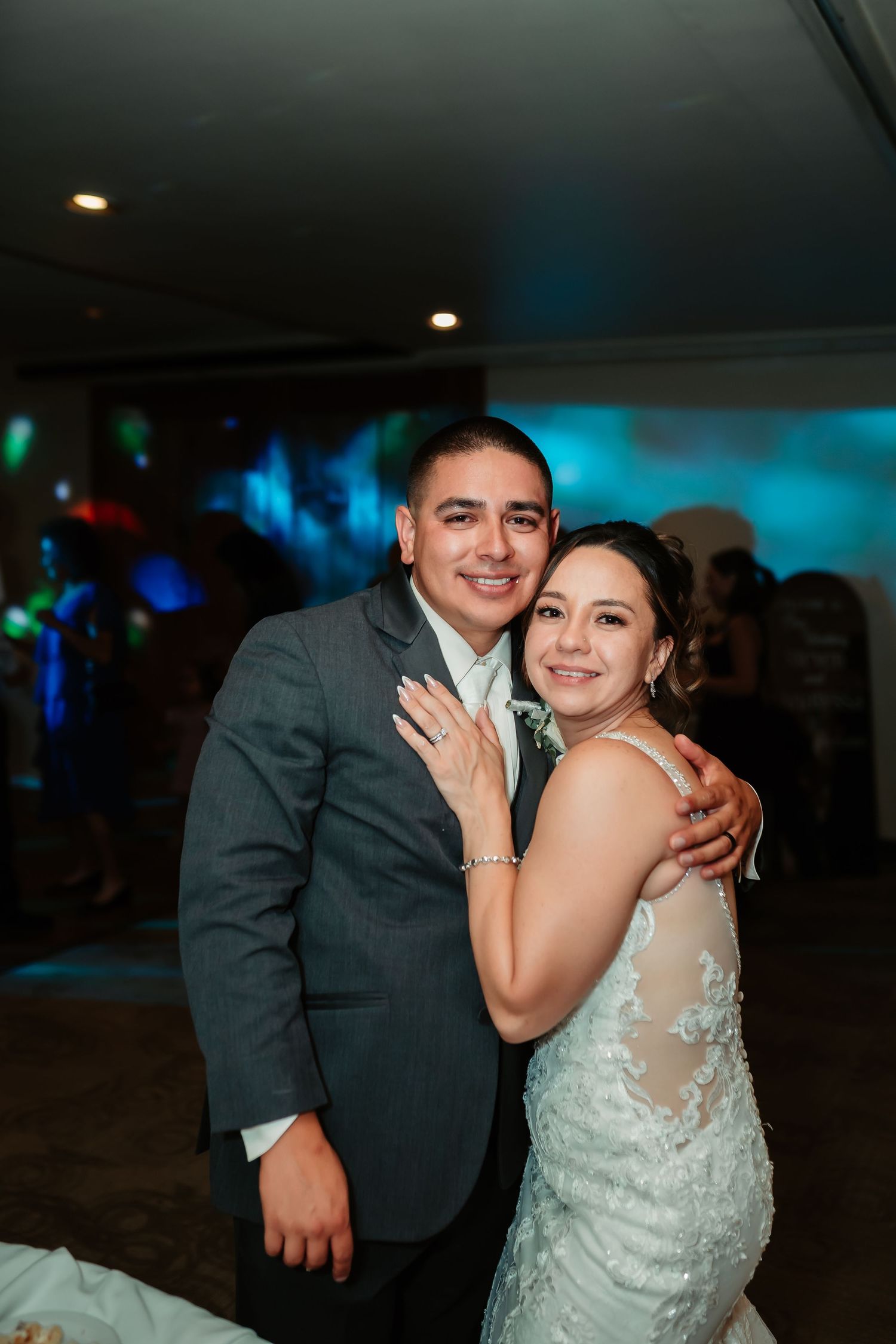 Couple embraces on dance floor with blue mood lighting at wedding reception.