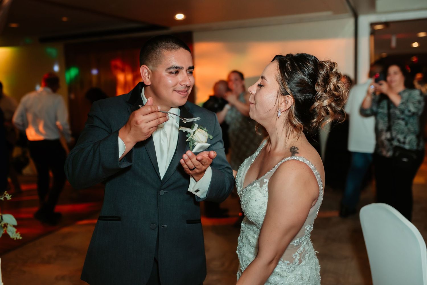Couple shares their wedding cake while smiling during their reception celebration.
