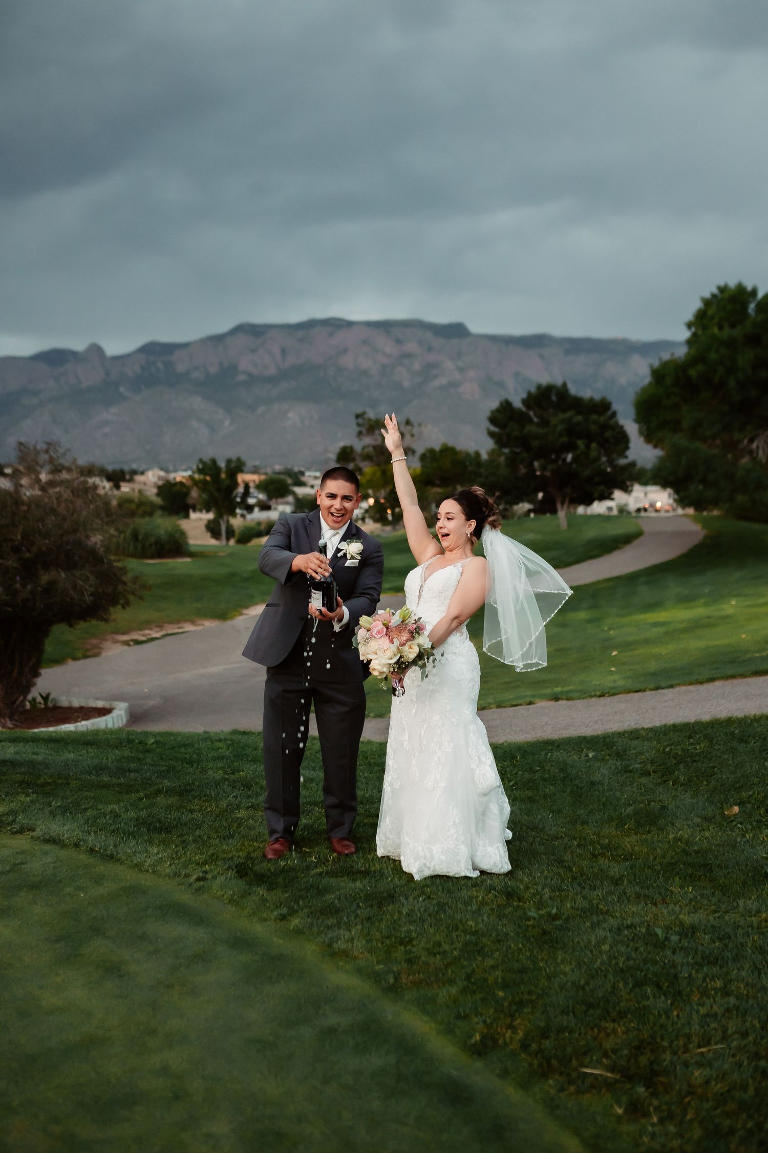 A wedding photoshoot on a grassy hill with mountains in the background under moody skies.
