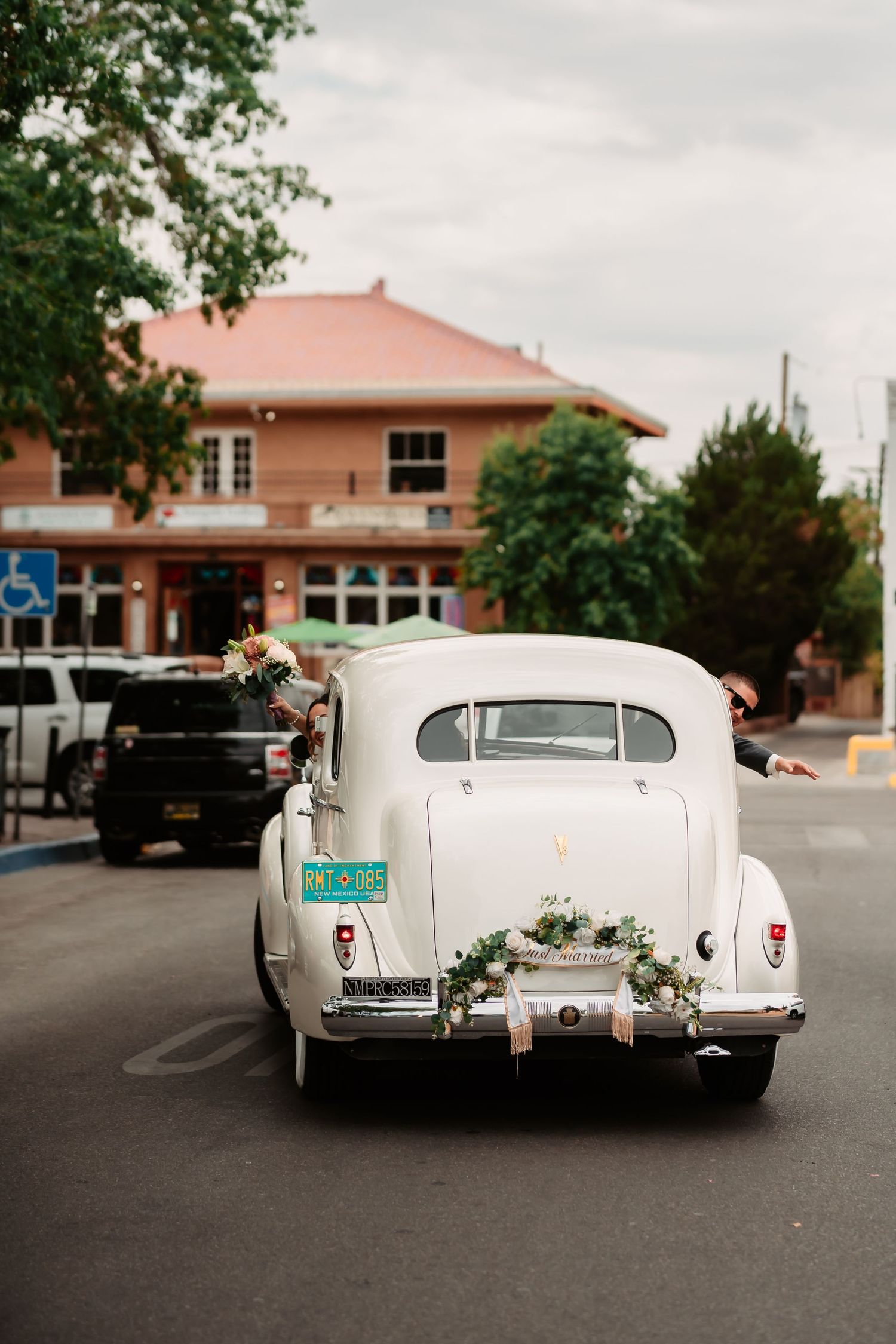 Rear view of decorated vintage white cars parked in front of pink adobe buildings.