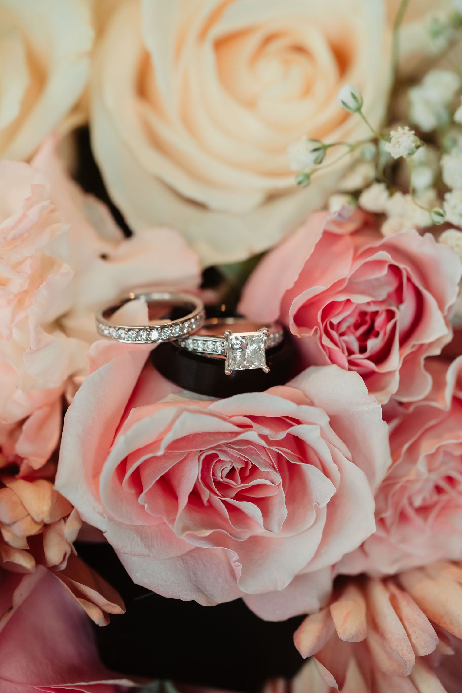 Close-up shot of diamond engagement ring nestled among soft pink and white roses.
