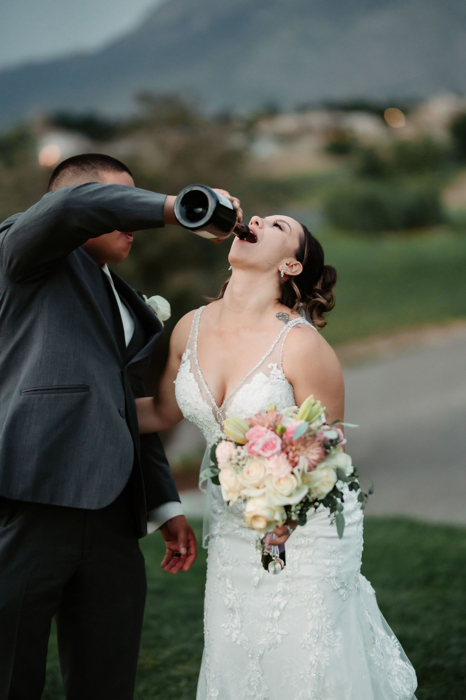 A newlywed couple takes celebratory drinks together on their wedding day outdoors.