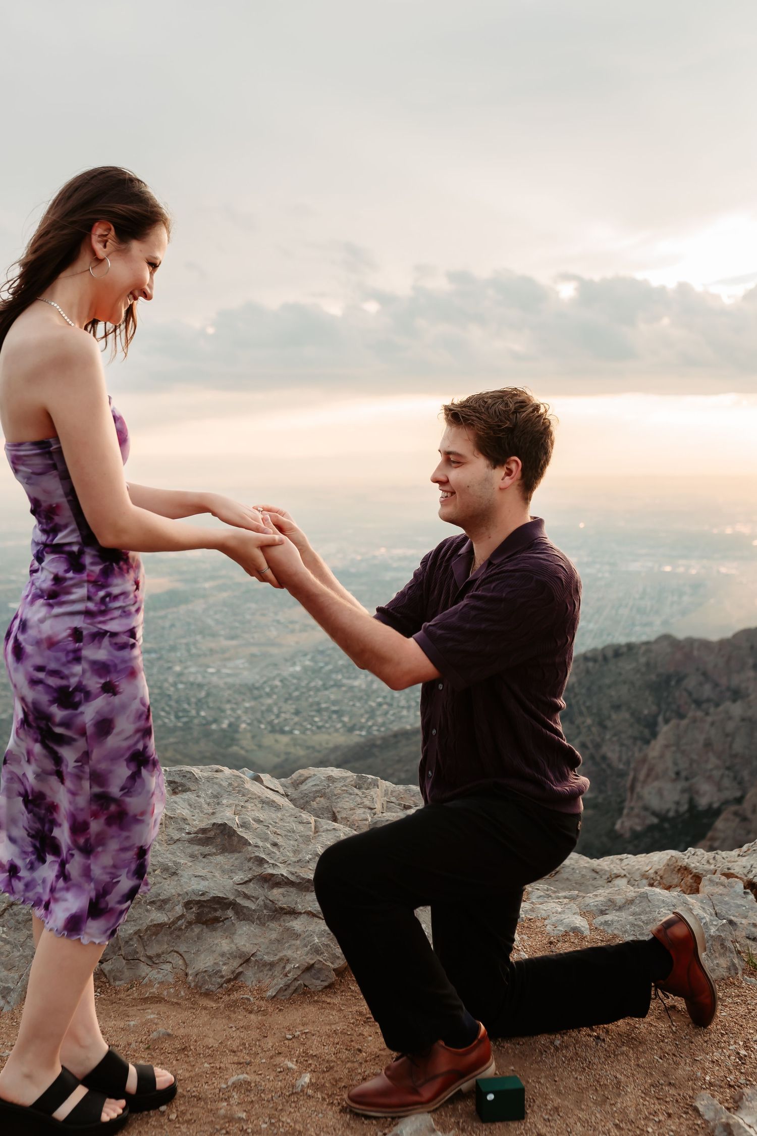 A romantic marriage proposal taking place on a scenic mountain overlook during sunset.