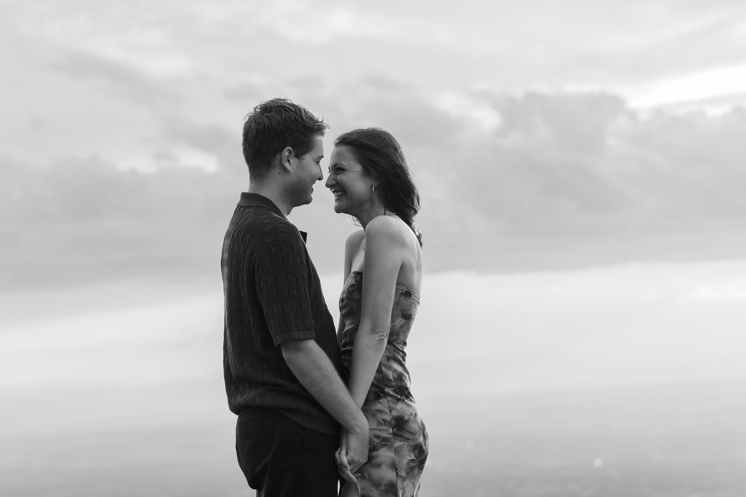 A romantic couple shares an intimate kiss against a moody black and white sky backdrop.