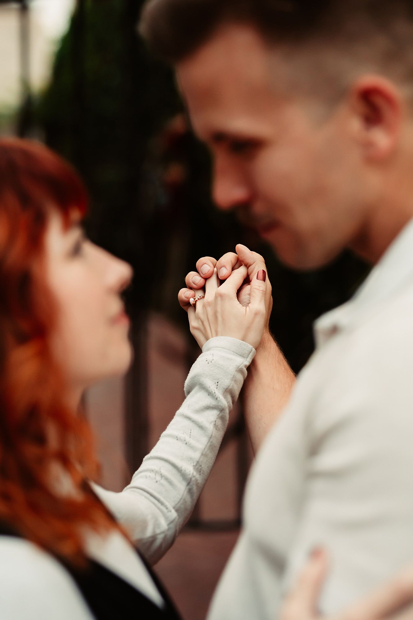 A romantic couple holding hands and gazing into each other's eyes, with the woman's red hair cascading softly.