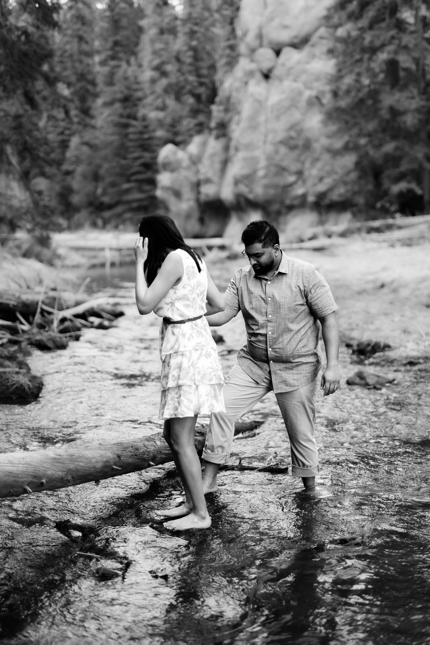 A black and white image of a couple walking through shallow water in a rocky landscape.