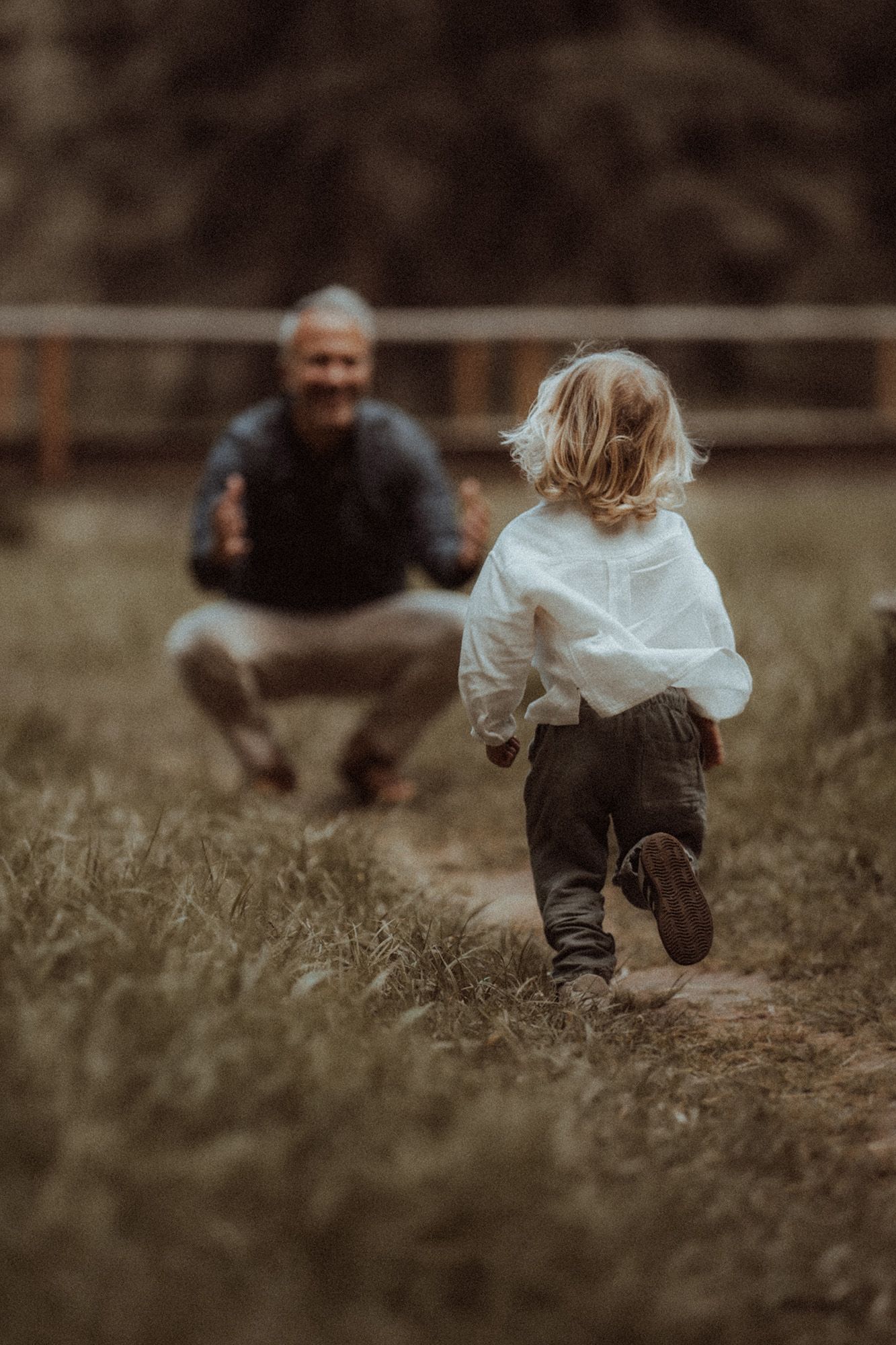 Young child running toward smiling man crouching on a grassy outdoor path.