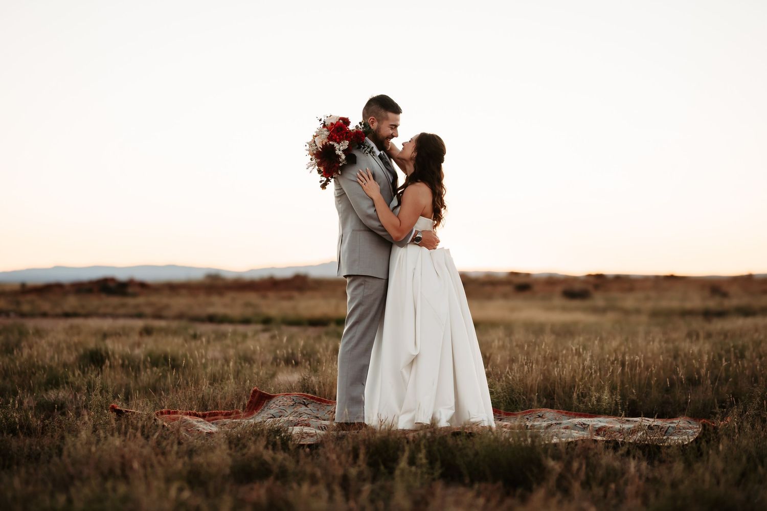 Romantic couple embraces in a golden field at sunset during a rustic outdoor wedding photoshoot.