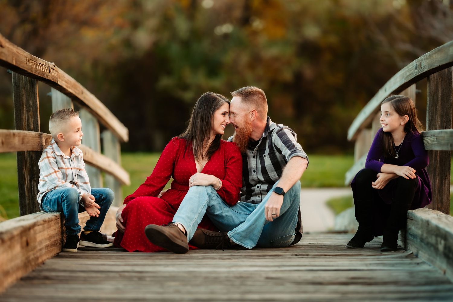 A romantic couple lying on a wooden deck surrounded by autumn foliage during an outdoor photo session.