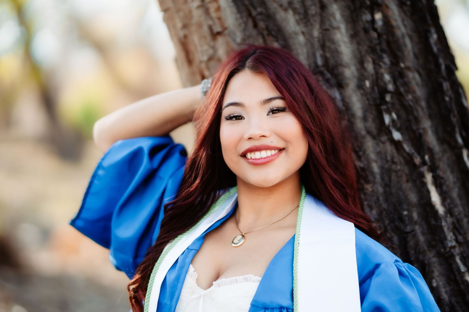 Close up portrait of graduate in blue and white academic regalia smiling outdoors.