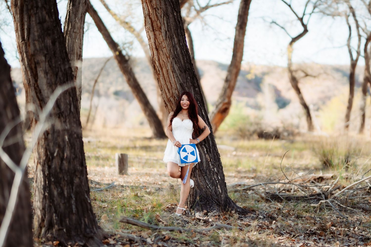 Natural light portrait in wooded area with person holding blue sign against mountain backdrop.
