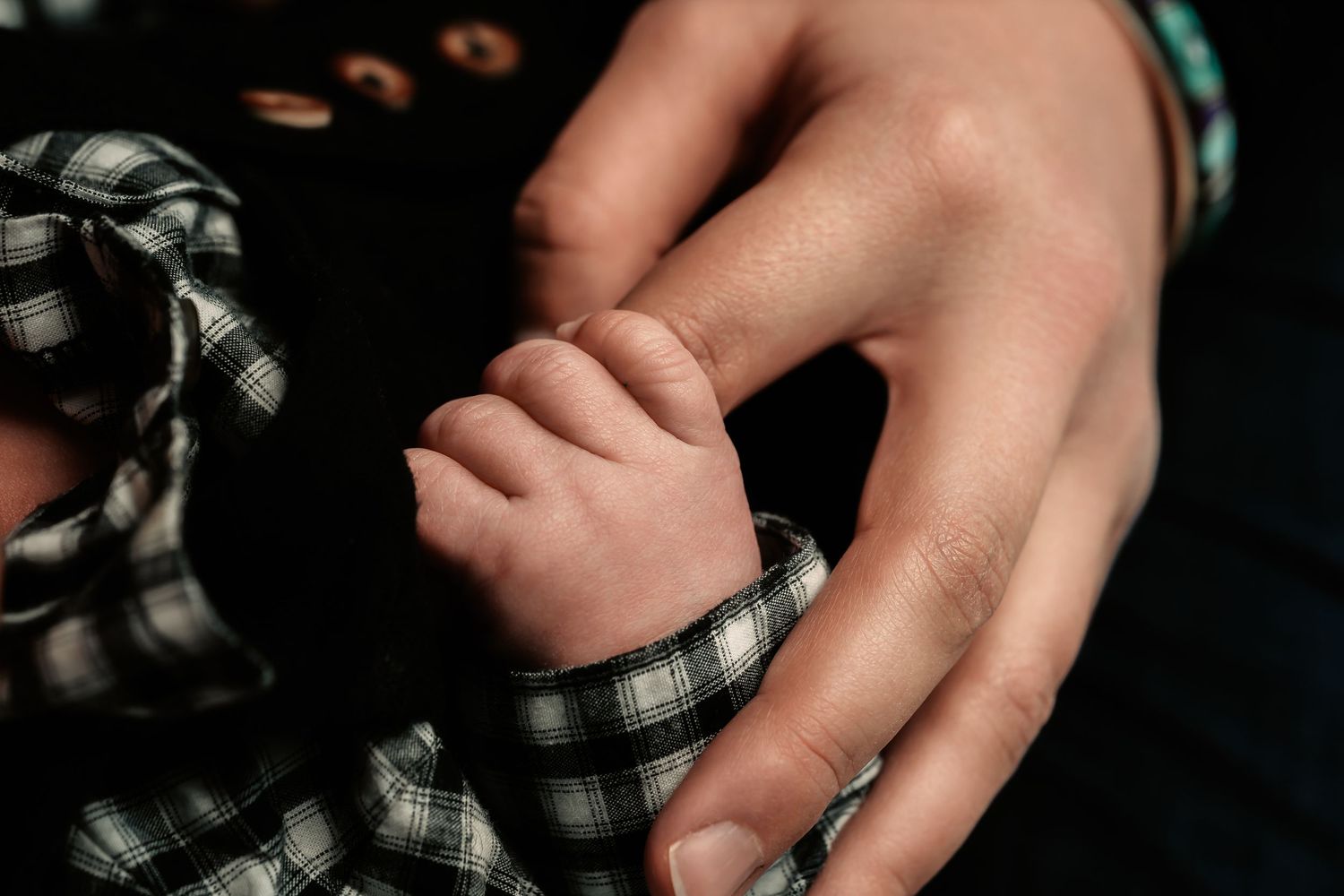 Close-up of hands holding a plaid patterned fabric in soft lighting against a dark background.