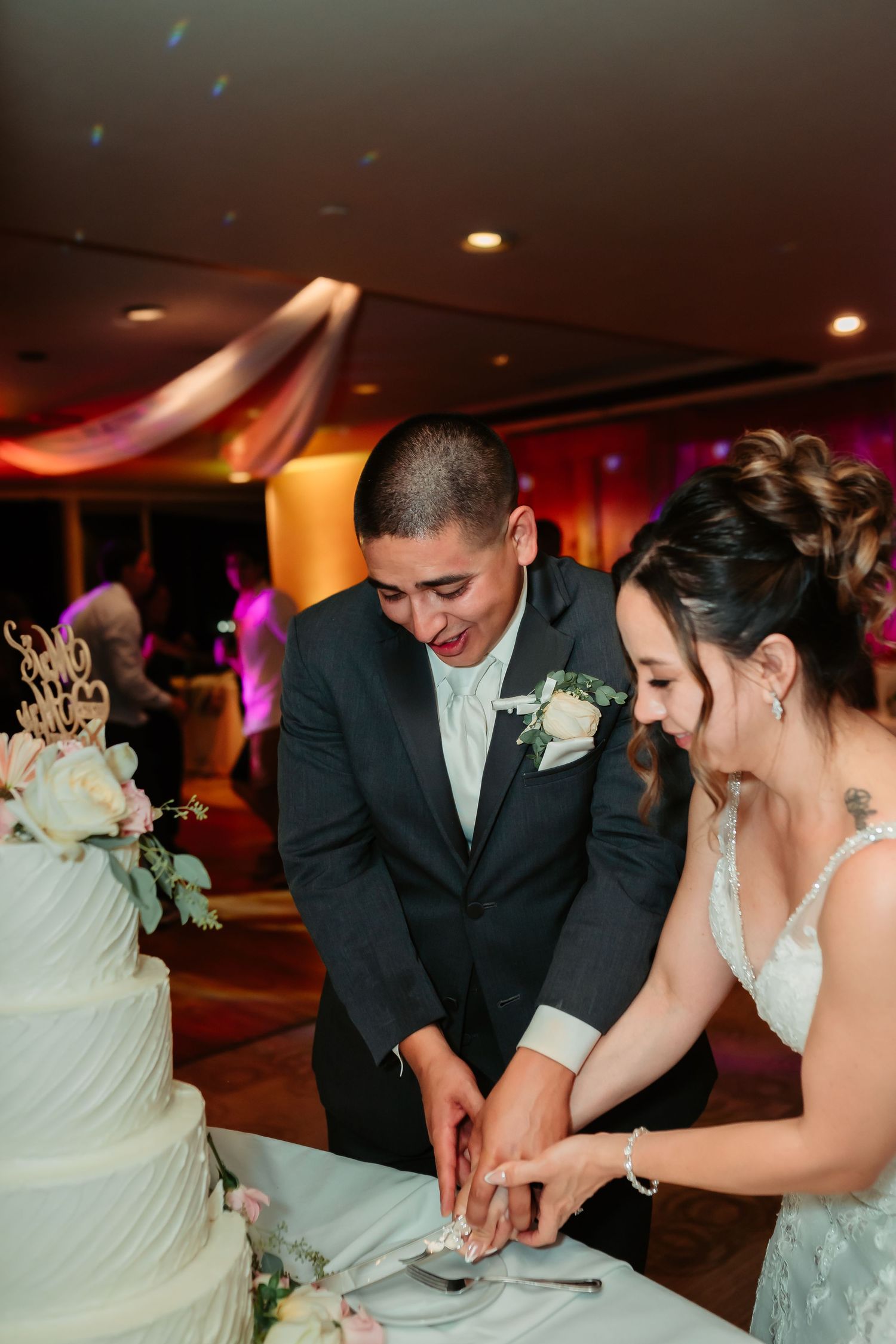 Couple cutting their multi-tiered white wedding cake at the reception.