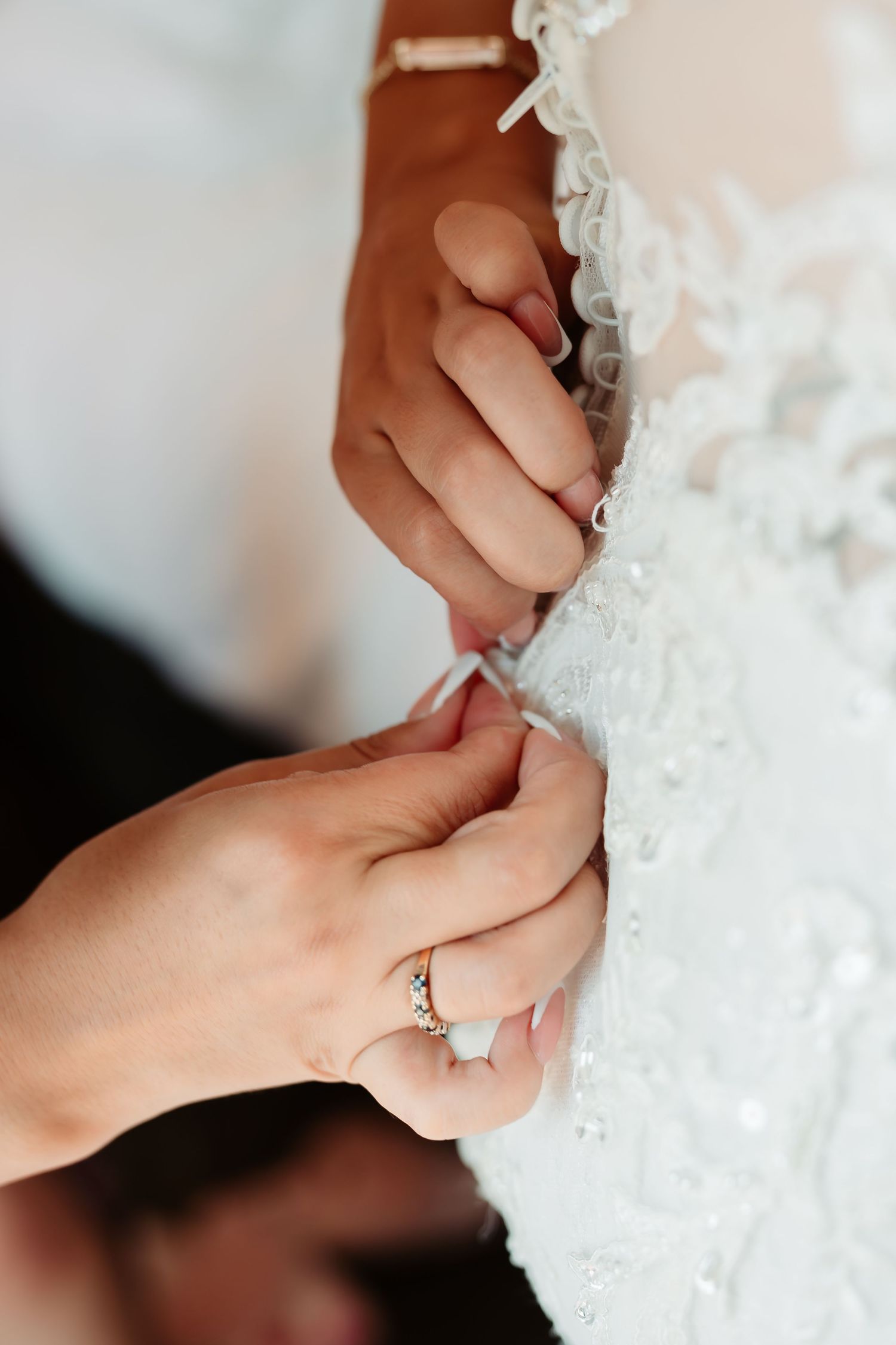 Close-up of hands delicately adjusting intricate lace details on a white wedding dress.