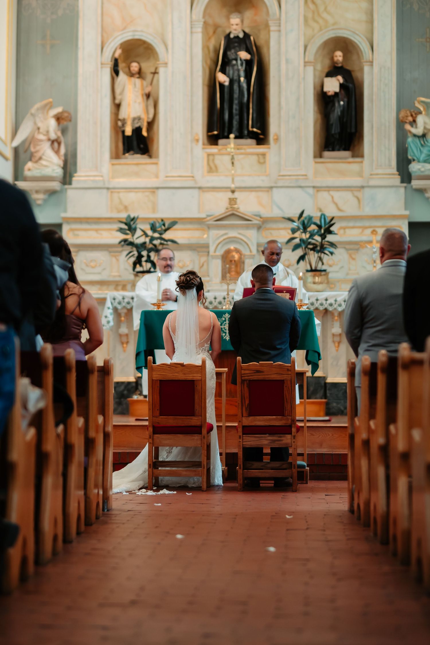 Church sanctuary with ornate altar, religious statues, and wooden pews during ceremony.