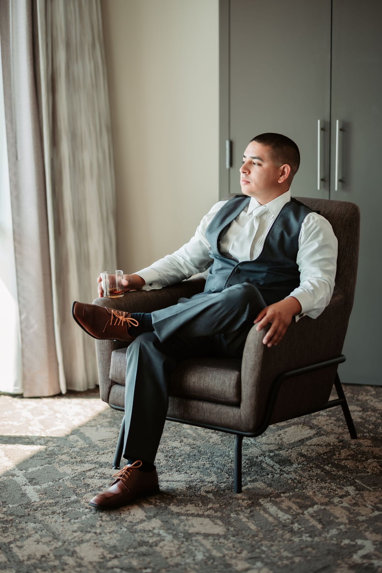 Series of relaxed poses in a gray armchair showing formal attire and brown leather shoes against patterned carpet.