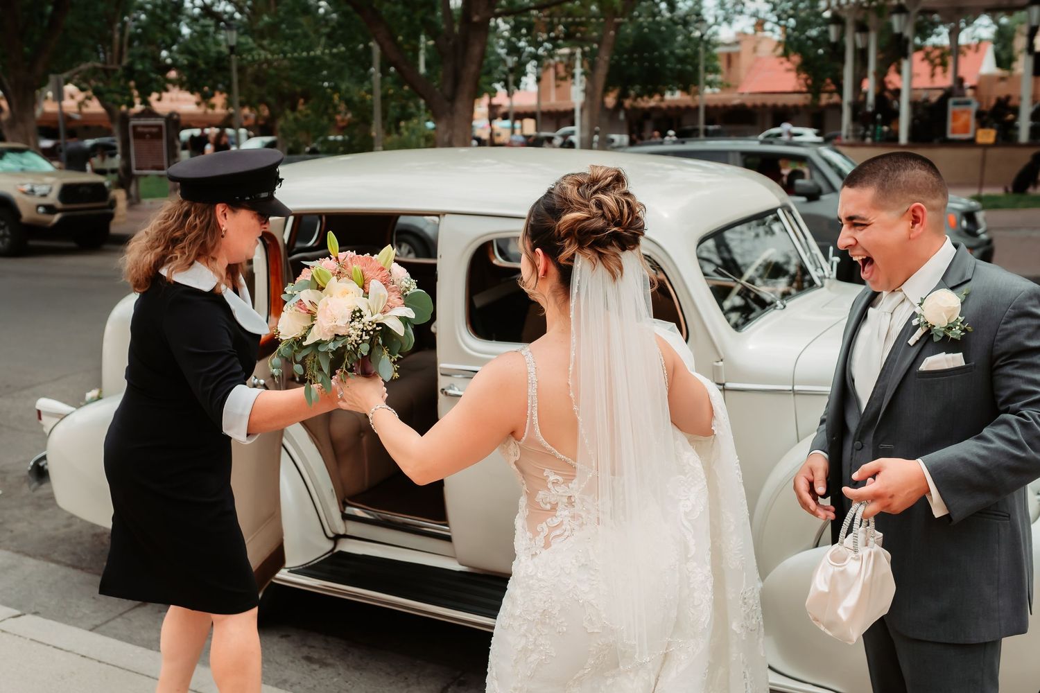 A wedding party gathers outside a vintage white car as they prepare for a celebratory send-off.