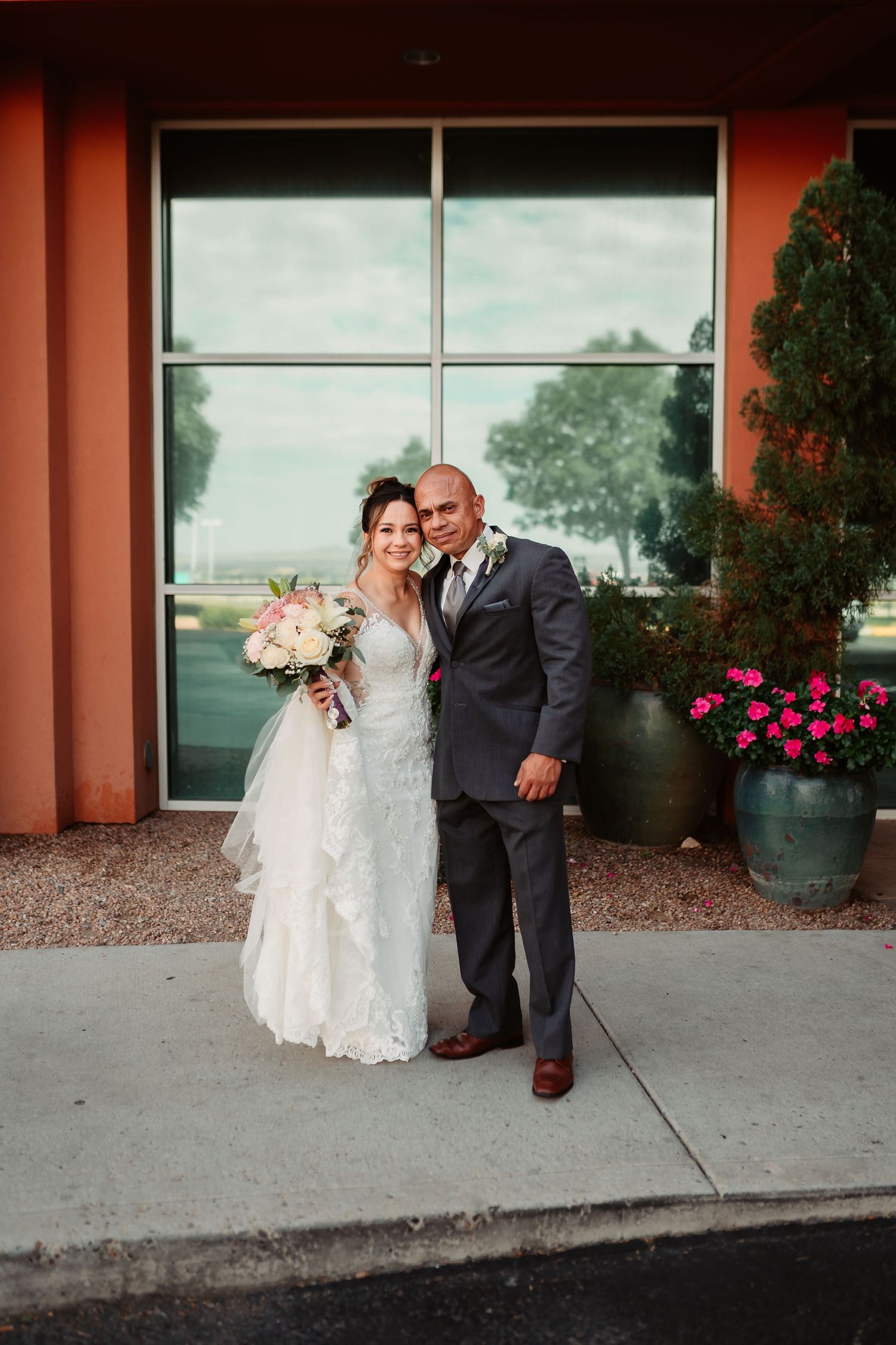 A sweet moment between newlyweds posing together against a coral stucco wall background.
