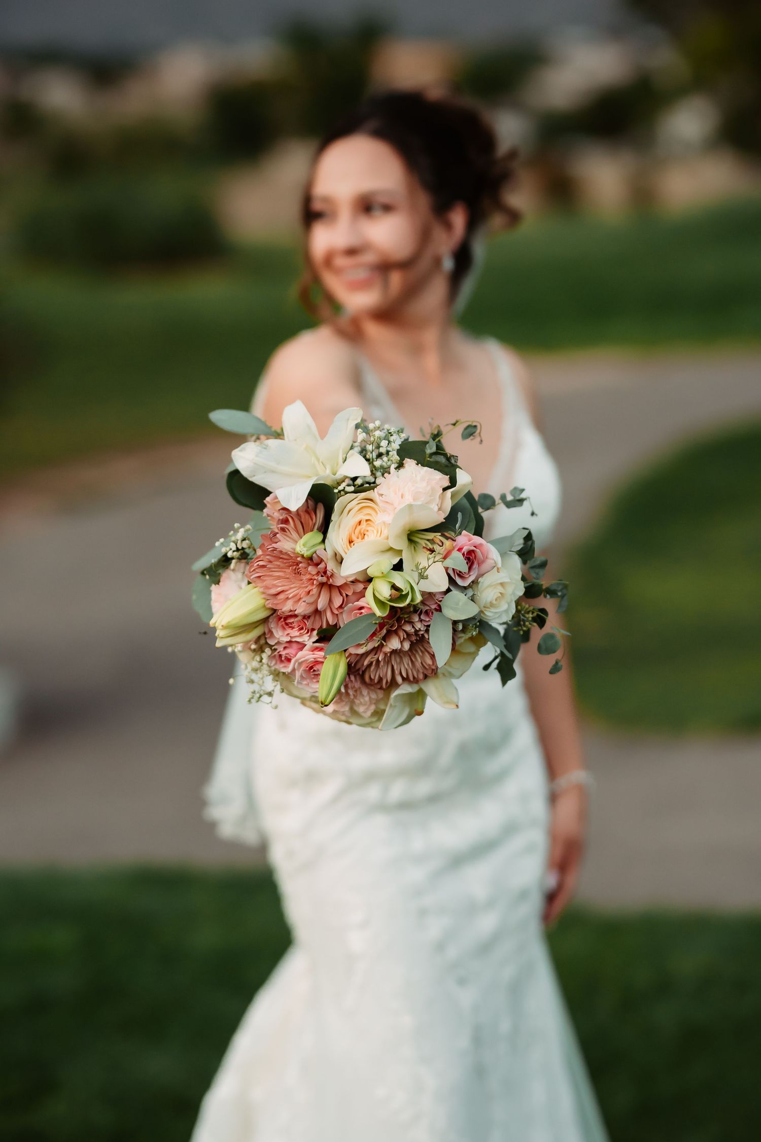 Beautiful bridal bouquet with peach and pink flowers against a white lace wedding dress.