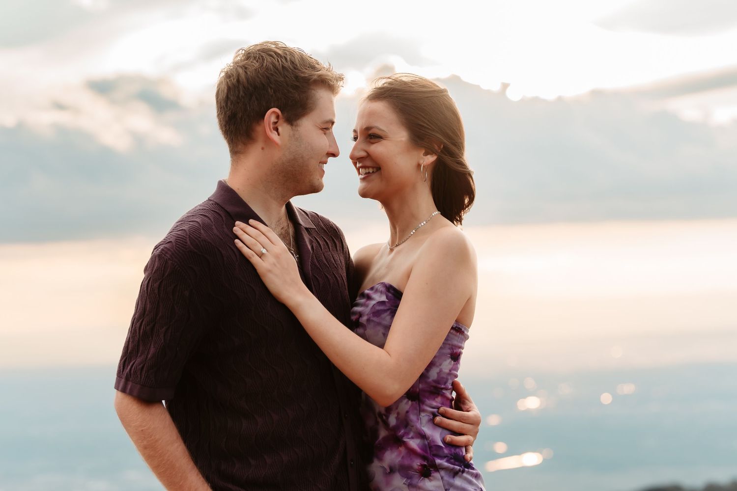 Two people share romantic moment together on mountaintop against soft cloudy sky.