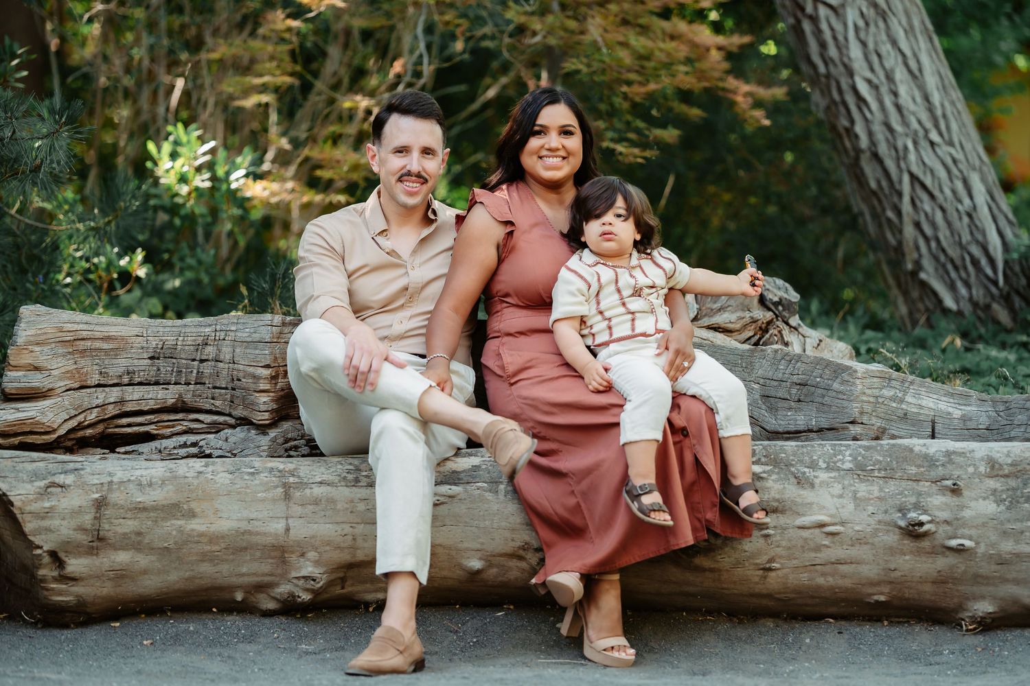 Family sitting together on fallen tree trunk at beach during sunset in coordinated rust and cream outfits.