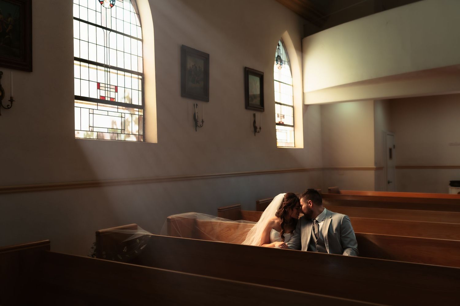 Sunlight streams through stained glass windows in an empty church sanctuary with wooden pews.