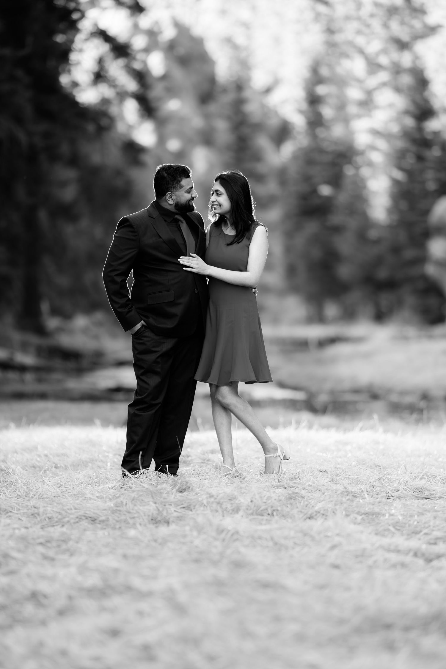 A black and white portrait of a couple sharing a playful moment in a forest clearing.