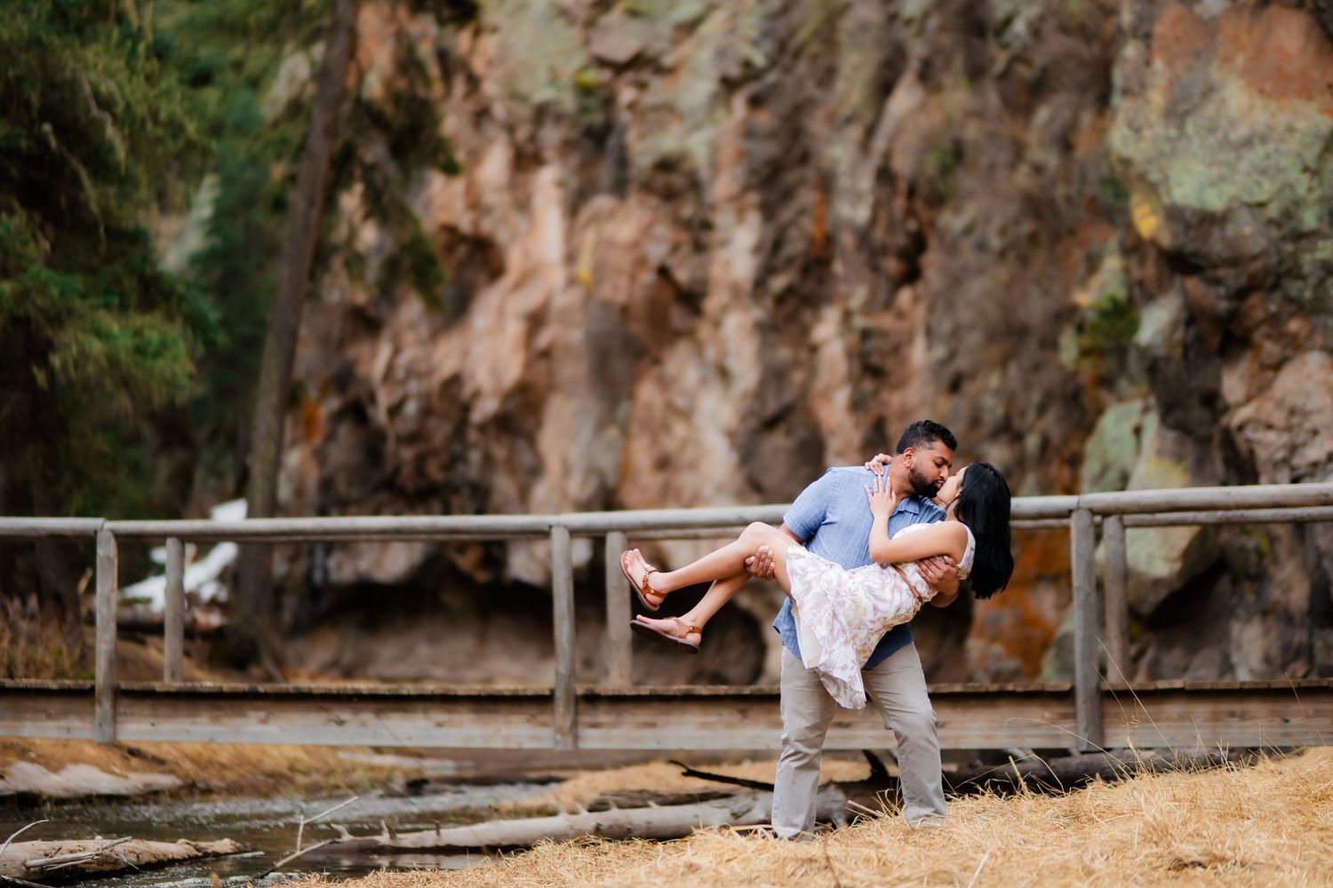 A couple shares a romantic dip pose on a wooden boardwalk with rocky cliffs in the background.
