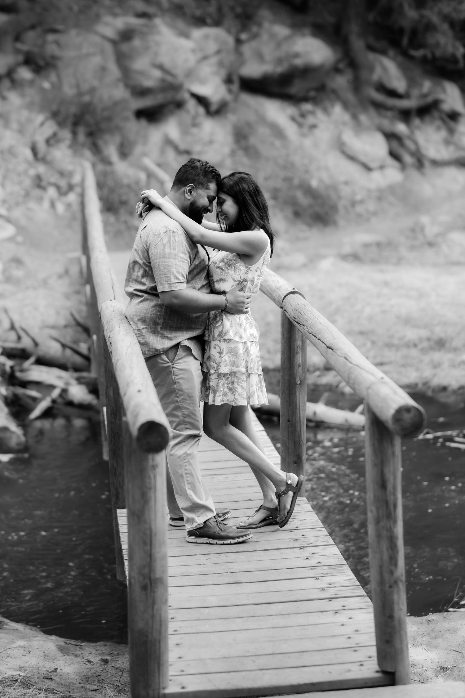 A romantic black and white moment captured on a wooden footbridge over water.