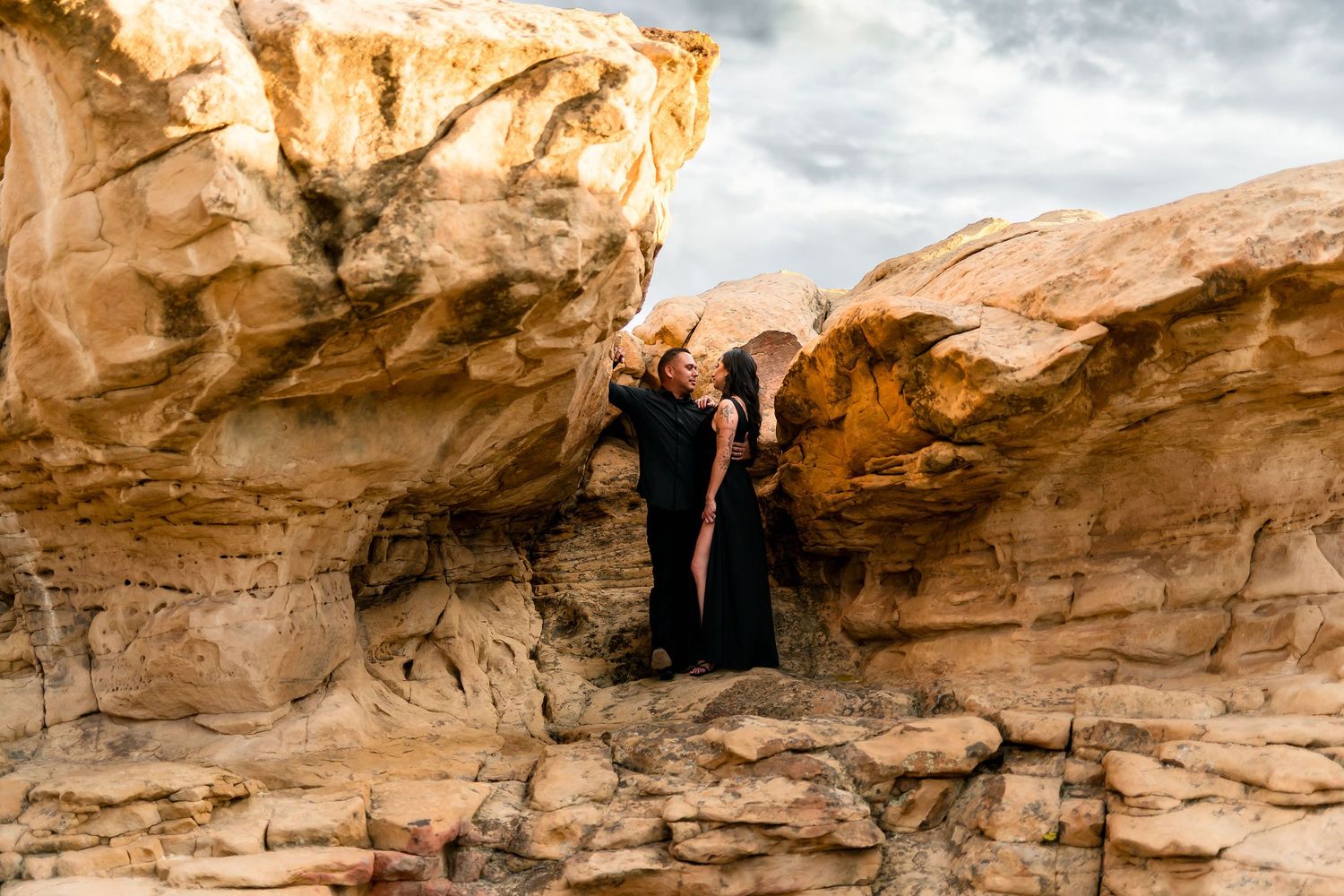 Couple embracing romantically between towering golden sandstone rock formations in a desert landscape.