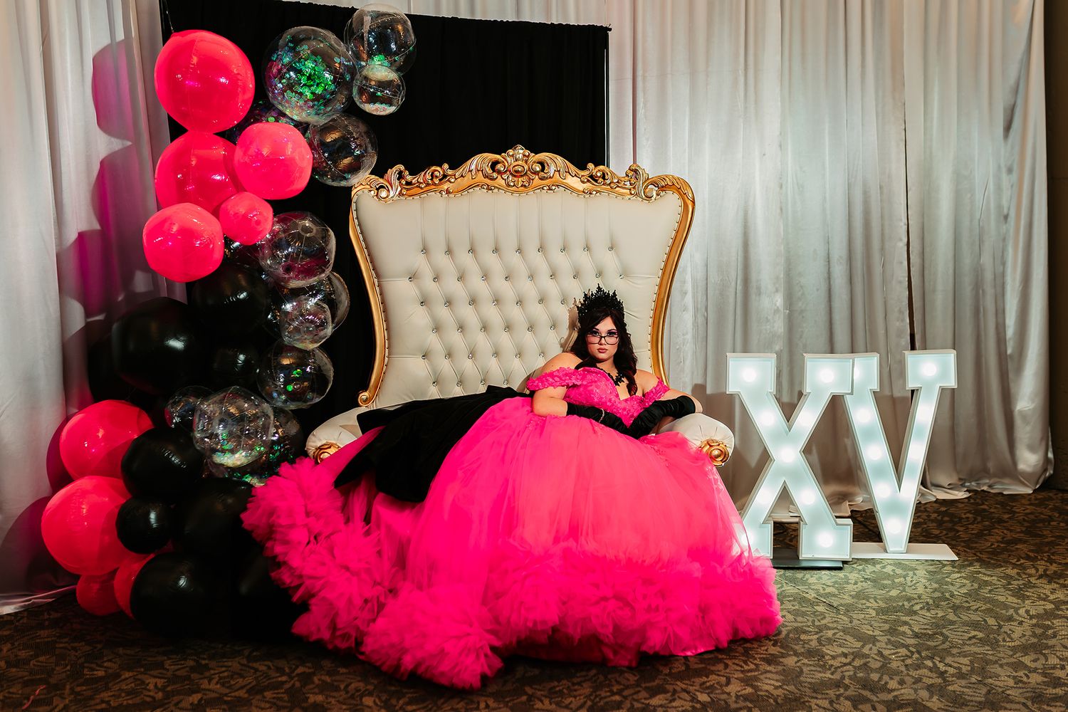 A pink and black quinceañera setup with a luxurious throne chair, balloons, and XV lettering display.