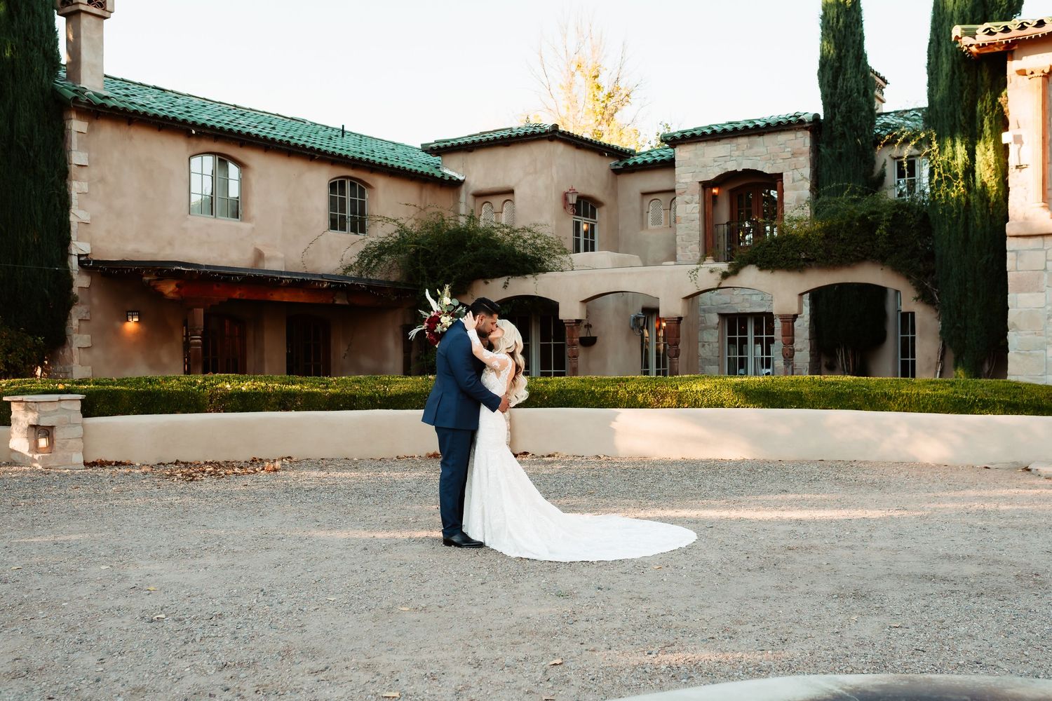 A romantic couple dances together at dusk in a rustic courtyard with stone buildings and warm lighting.