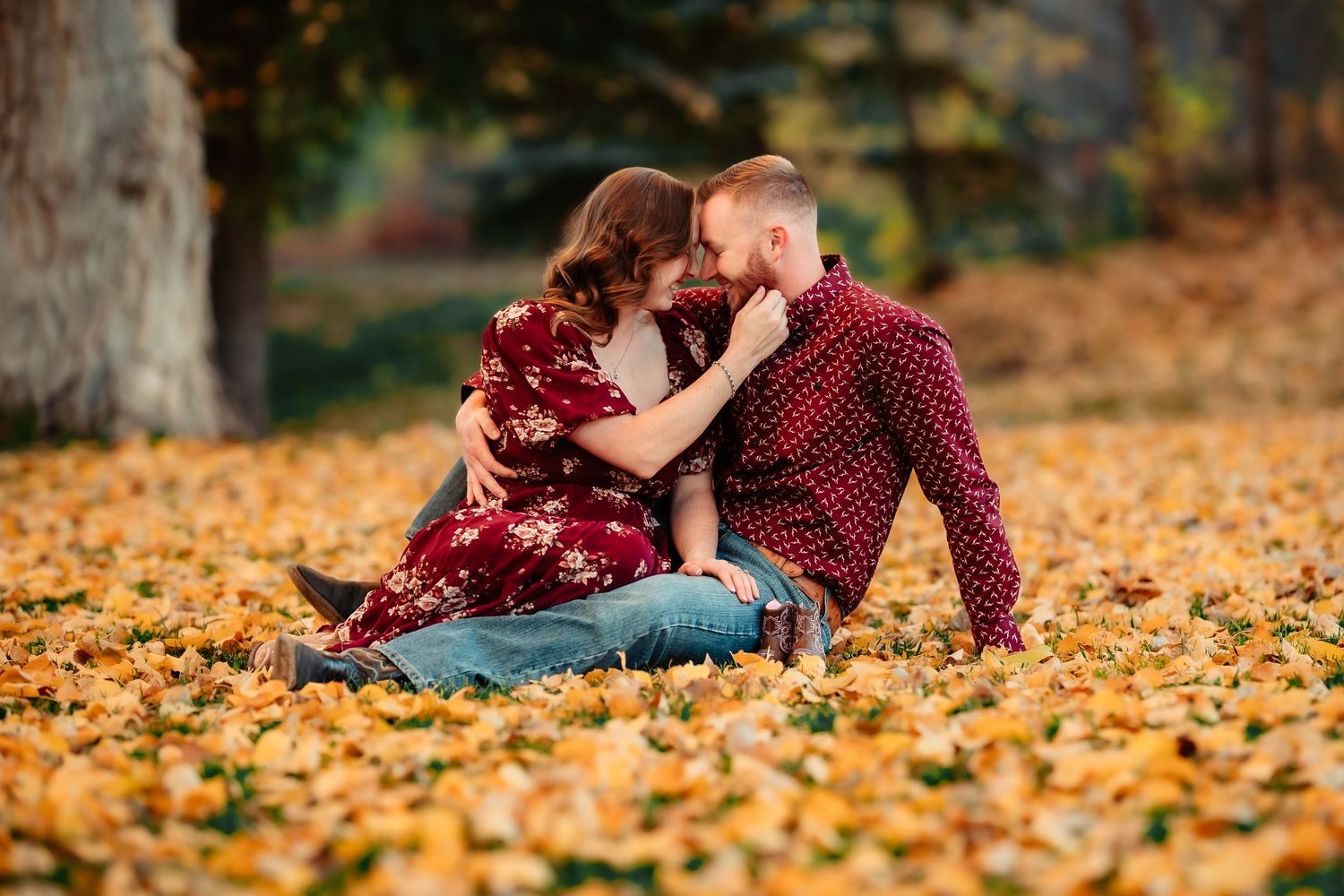 A couple shares a romantic moment while lying in colorful autumn leaves on the ground during fall.
