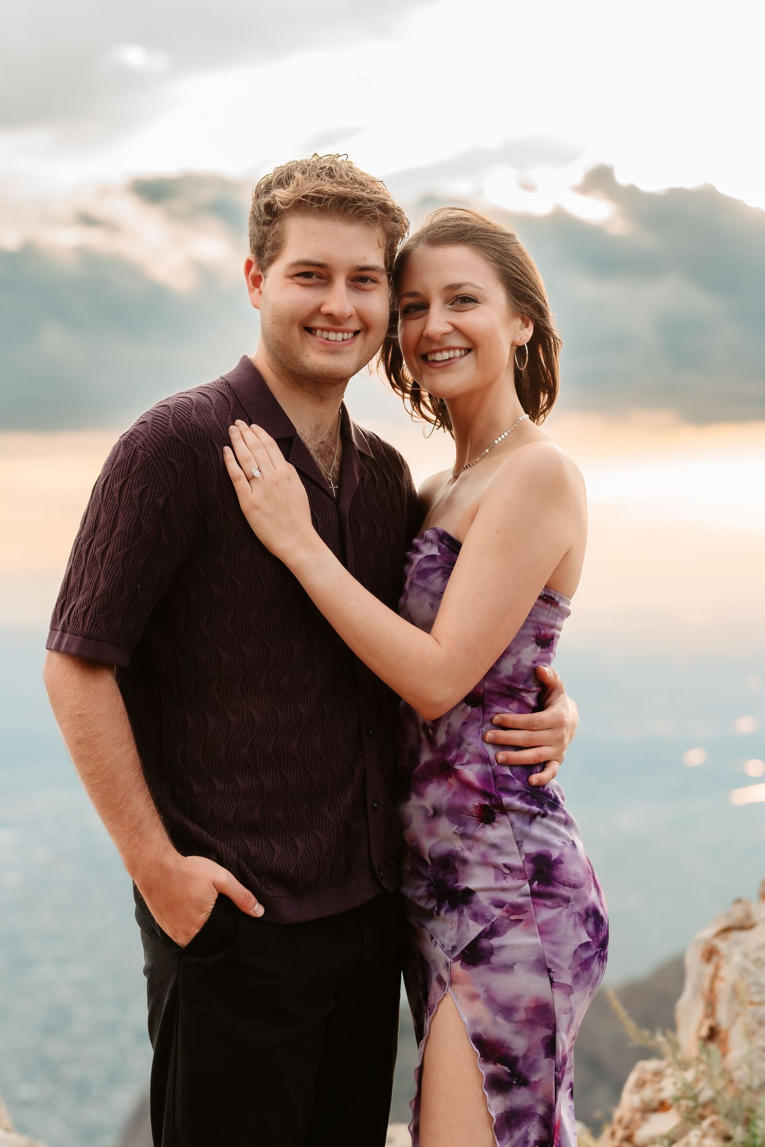 A couple embracing and celebrating their engagement on a mountain cliff during golden hour.