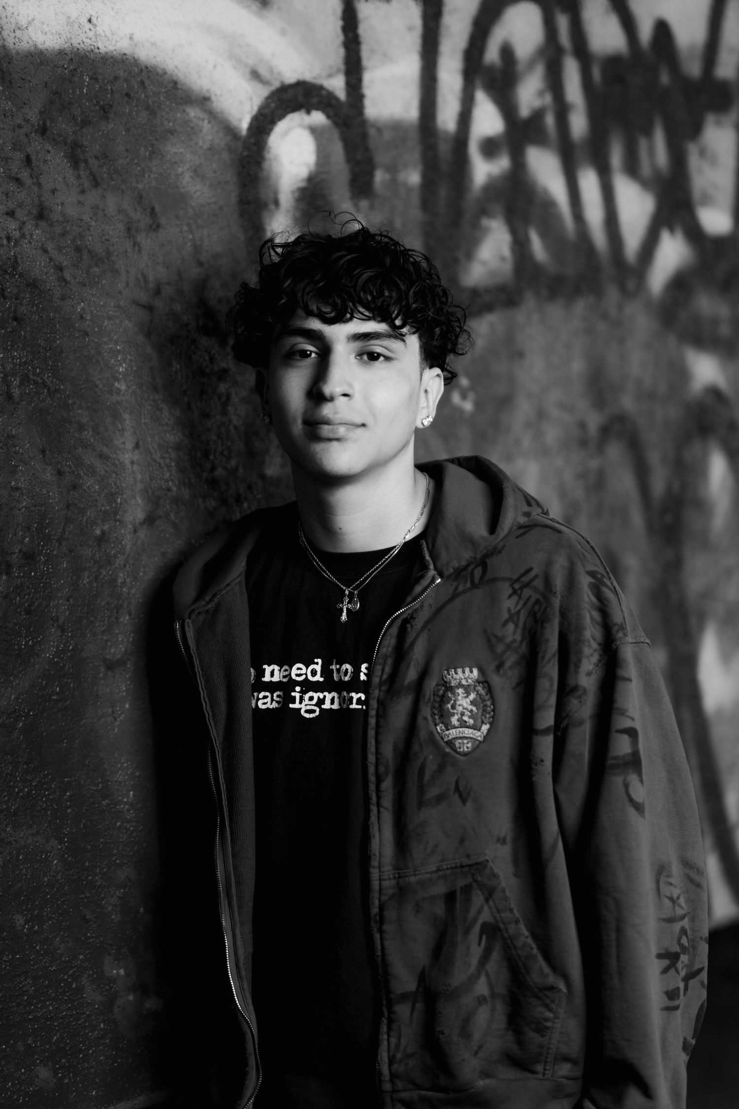 Monochromatic portrait against graffiti wall featuring dark hoodie and urban style.