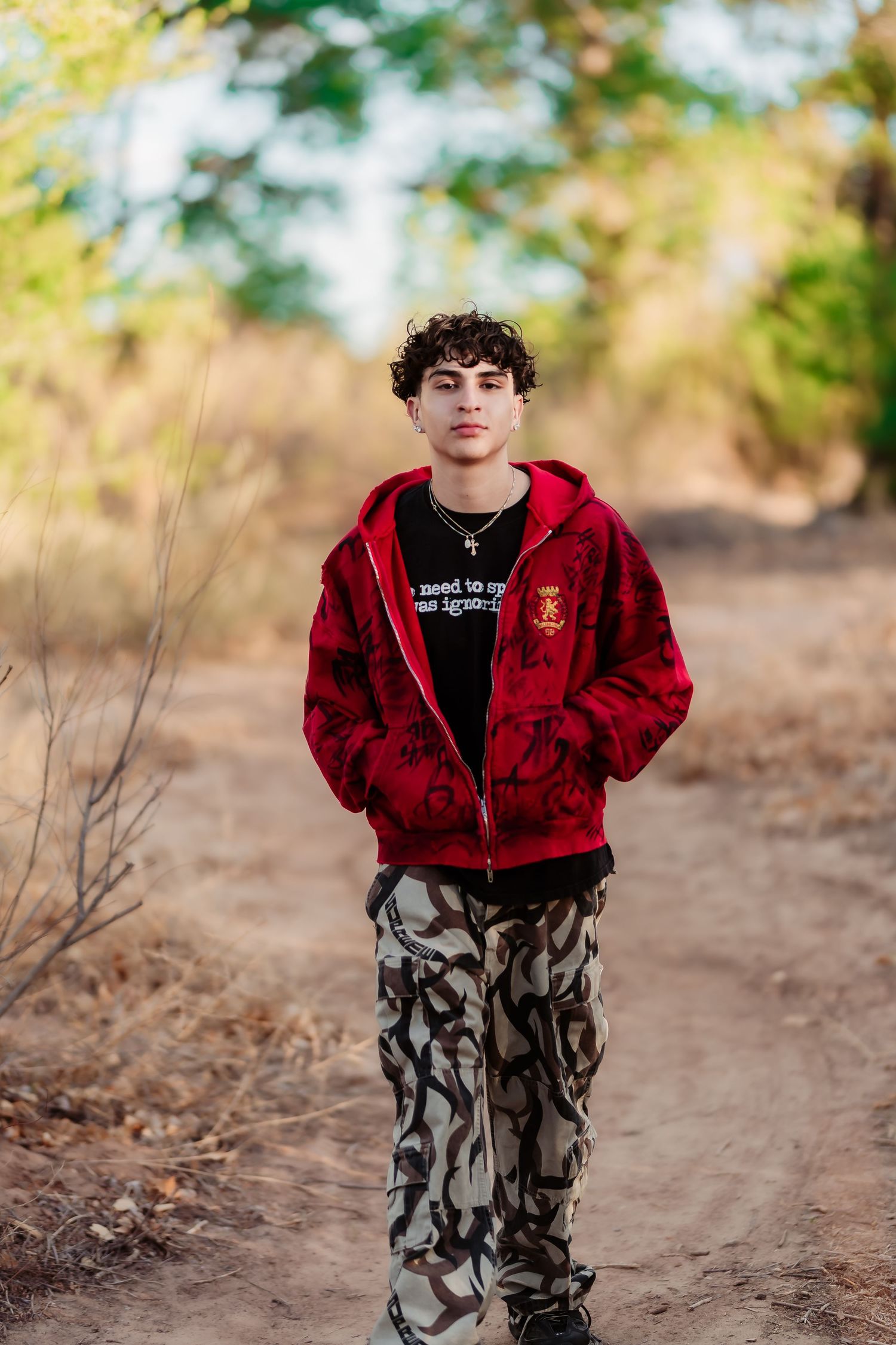 Portrait on a nature path featuring someone wearing a red zip-up hoodie and camouflage pants.