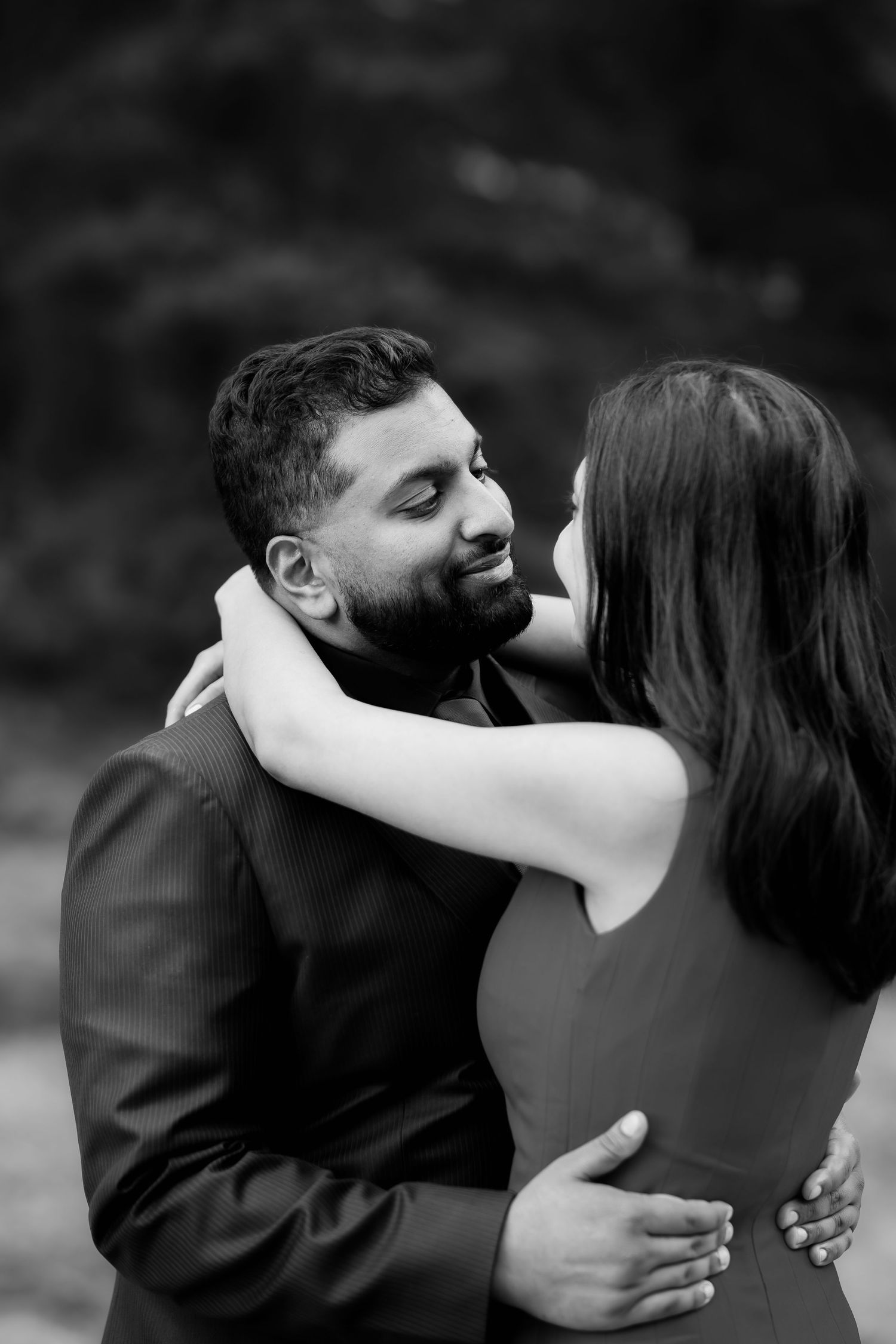 An intimate black and white portrait of a couple embracing outdoors.
